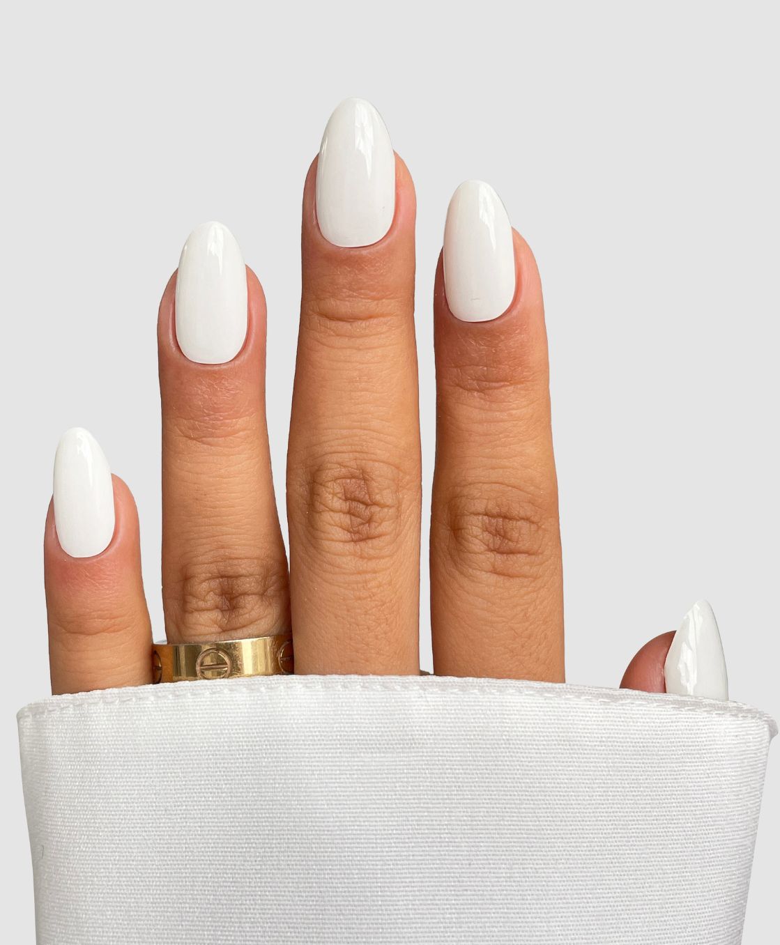A hand with Sassy Saints' Coconut Milk Gel Wrap manicured nails rests against a light background. A gold ring adorns the middle finger, while a white sleeve covers the wrist.