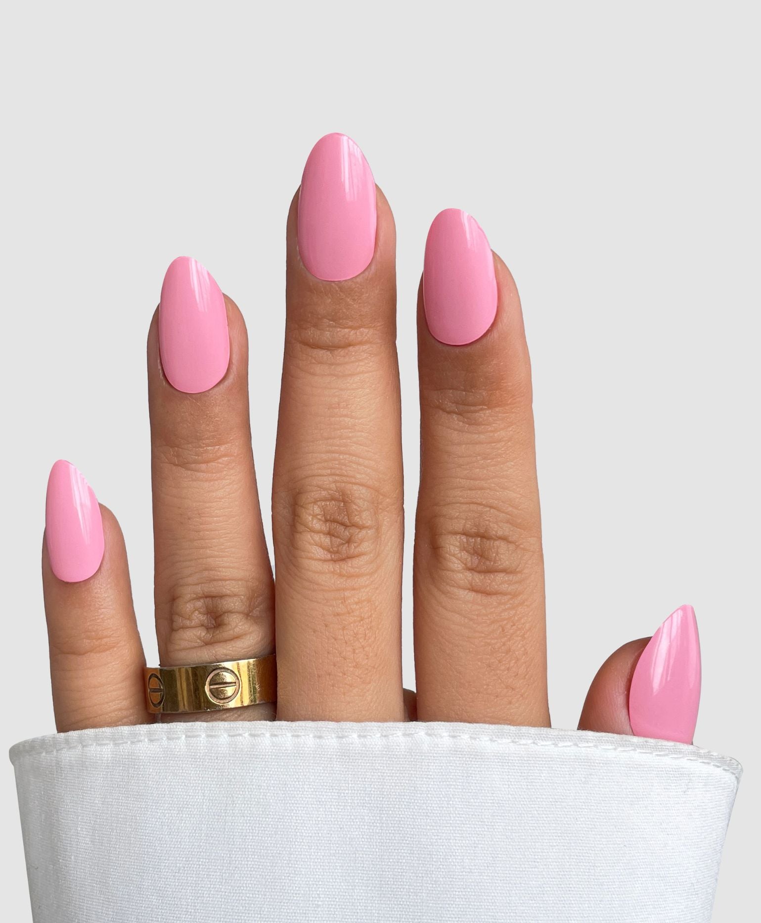 A hand with neatly manicured nails featuring Sassy Saints - Brings The Salon Home Sugar Candy Gel Wrap peeks from a white sleeve, gold ring on the middle finger, against a plain light gray background.