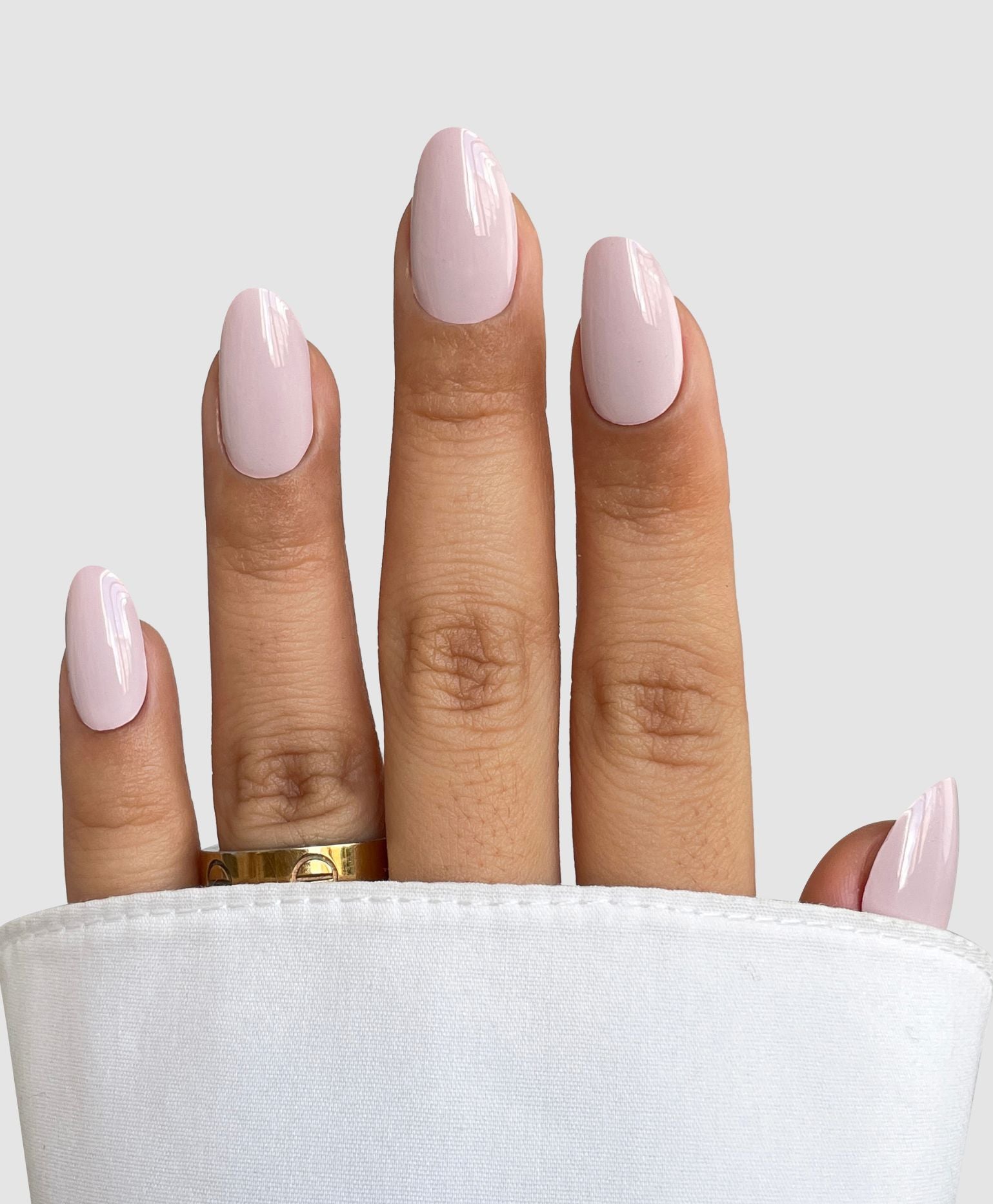 A hand with neatly manicured nails in a glossy pale pink shade, showcasing Sassy Saints' Soft Tulle Gel Wrap, wears a gold ring and is partially covered by a white sleeve against a light background. Brings The Salon Home.