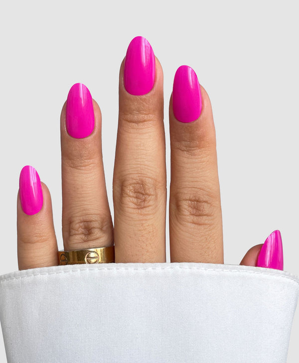 A hand showcases Sassy Saints’ Pink Hype Gel Wrap with a gold ring, partially covered by a white cuff, set against a plain light gray background.