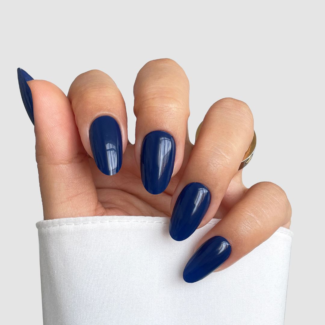 A hand with long, almond-shaped nails styled in Sassy Saints' Blue Eclipse Gel Wrap, partially covered by a white sleeve, set against a light gray background.