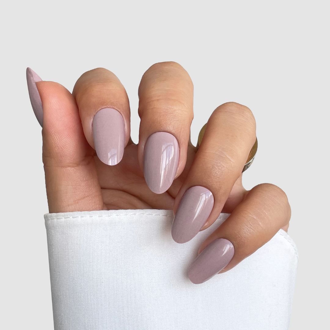 A hand with long, almond-shaped nails features Sassy Saints' Neutral Flow Gel Wrap, in a glossy light mauve shade, partially covered by a white sleeve against a plain light gray background.
