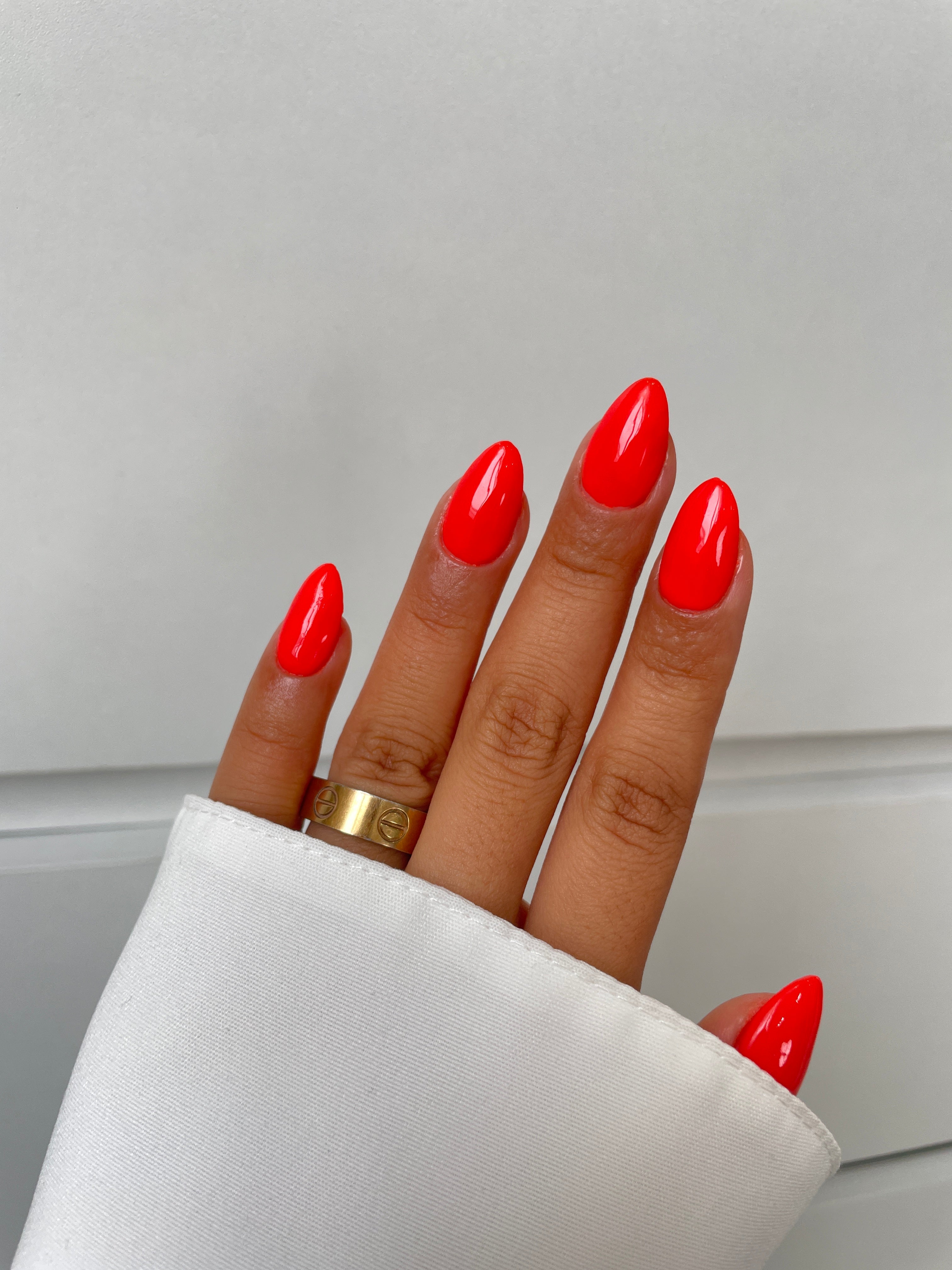 A hand with long, almond-shaped nails painted in Sassy Saints' Tropical Tease Dipping Powder wears a gold ring, shown against a white background with a white sleeve partially covering the wrist. Brings The Salon Home.
