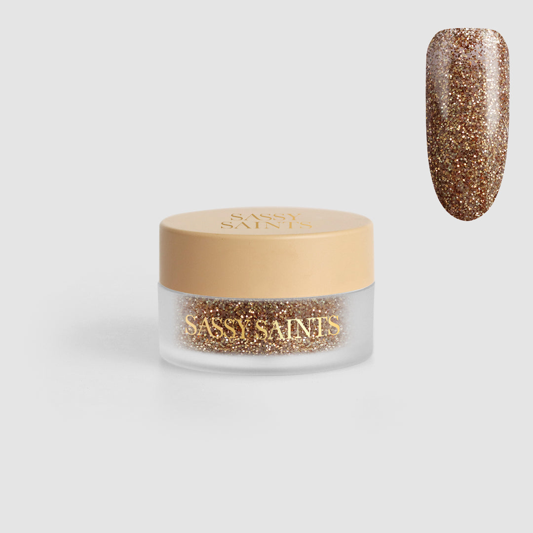 A small jar of Golden Gift Dipping Powder from Sassy Saints - Brings The Salon Home, filled with gold glitter powder and shown alongside a nail swatch displaying its glittery gold effect.