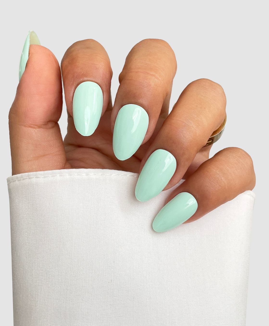 A hand with long, almond-shaped nails in Sassy Saints' Mint To Be Gel Wrap, a glossy pastel mint green, partially covered by a white sleeve against a light gray background.