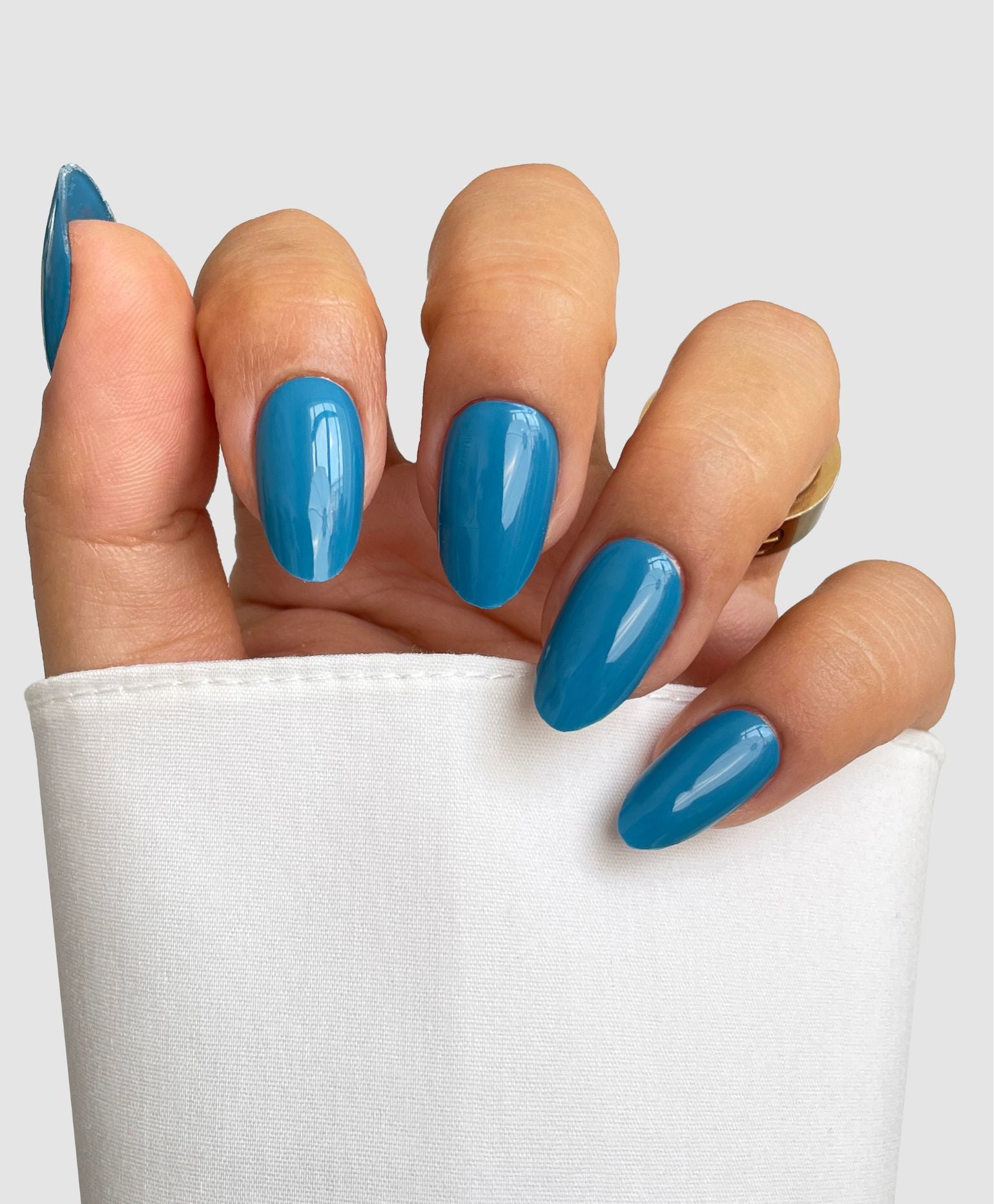 A hand with neatly manicured nails wearing Sassy Saints' Tonal Drift Gel Wrap, partially wrapped in white fabric, is set against a light gray background.