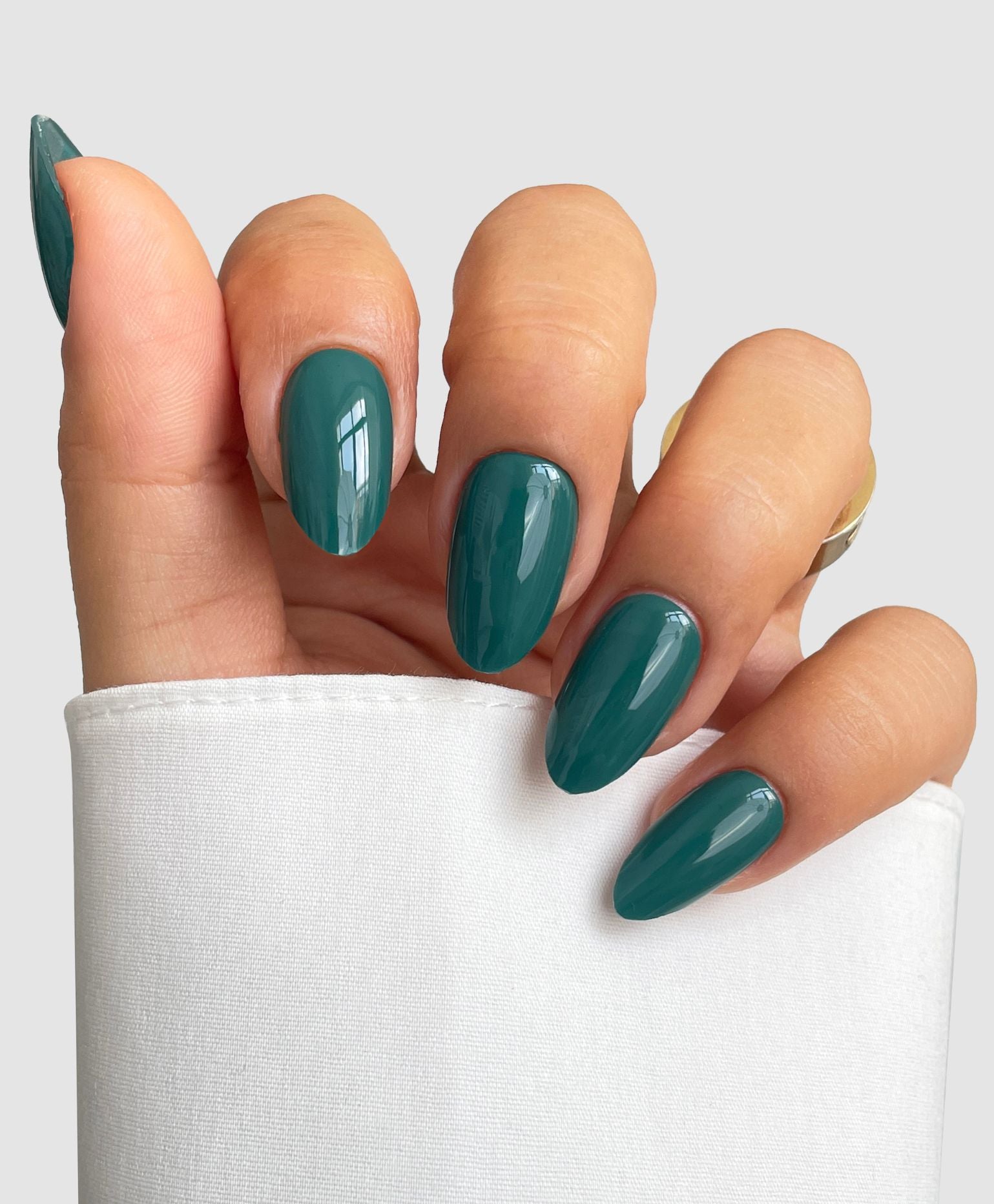 A hand with almond-shaped nails features the Sassy Saints Forest Green Gel Wrap, partially wrapped in a white sleeve, set against a light gray background.