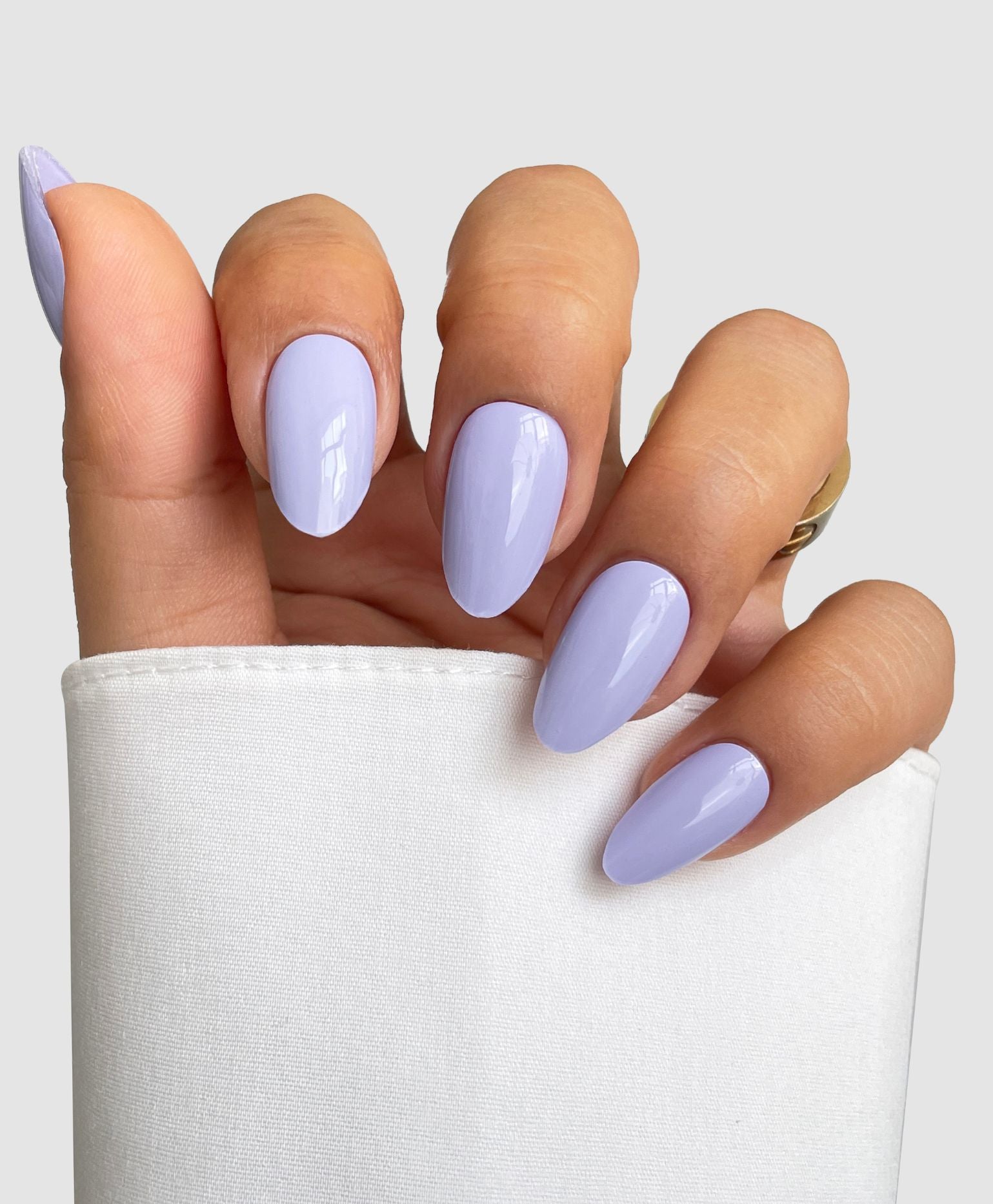 A hand with long, almond-shaped nails in Sassy Saints' Lavender Blush Gel Wrap, partially covered by a white sleeve, set against a light gray background.
