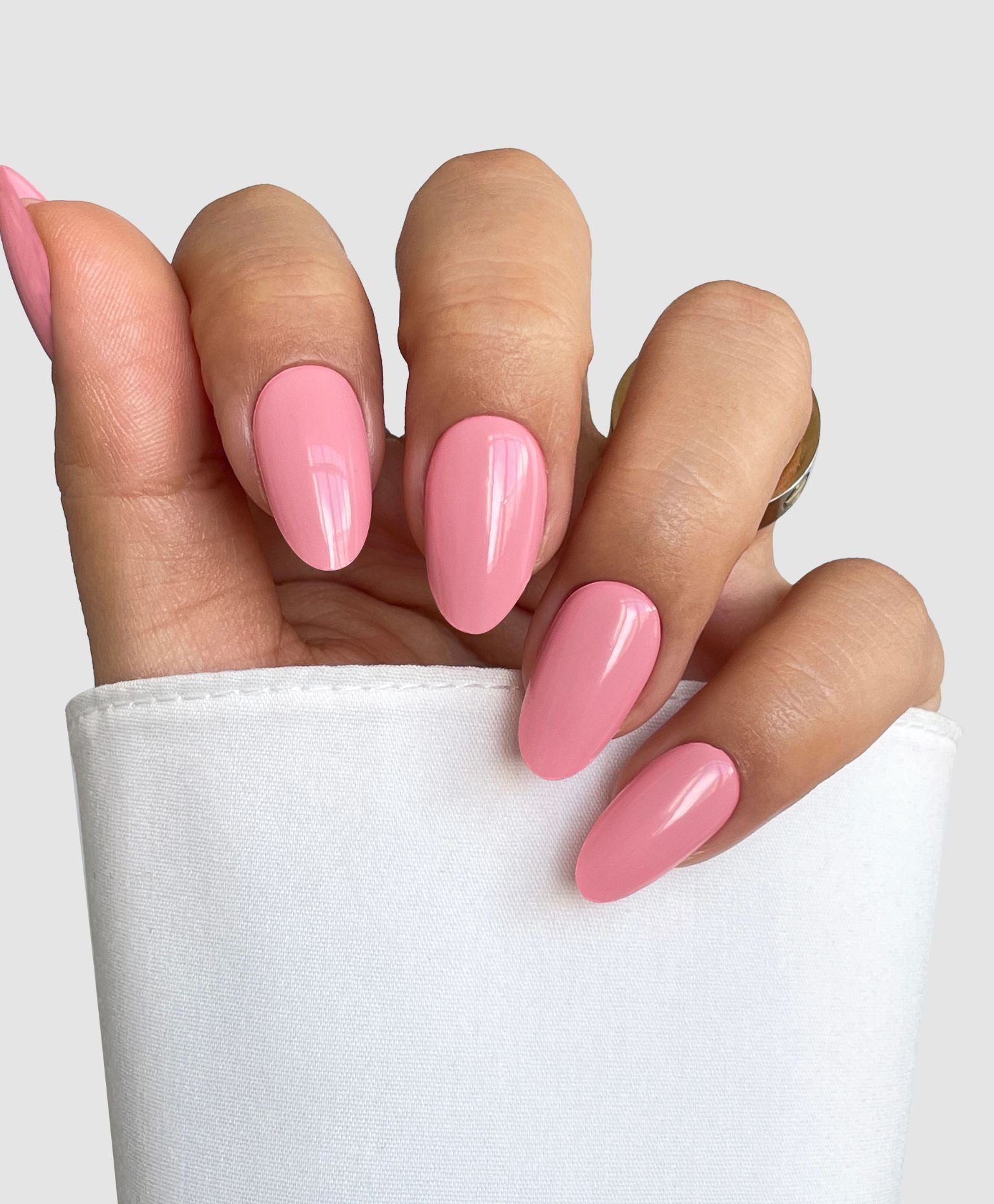 A hand with long nails wearing Sassy Saints - Brings The Salon Home's Rose Tone Gel Wrap, paired with a white shirt.