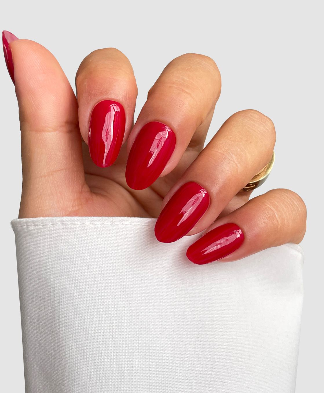 A hand with almond-shaped nails wears Sassy Saints’ Red Alert Gel Wraps, glossy red and partially covered by a white sleeve, set against a plain light gray background.