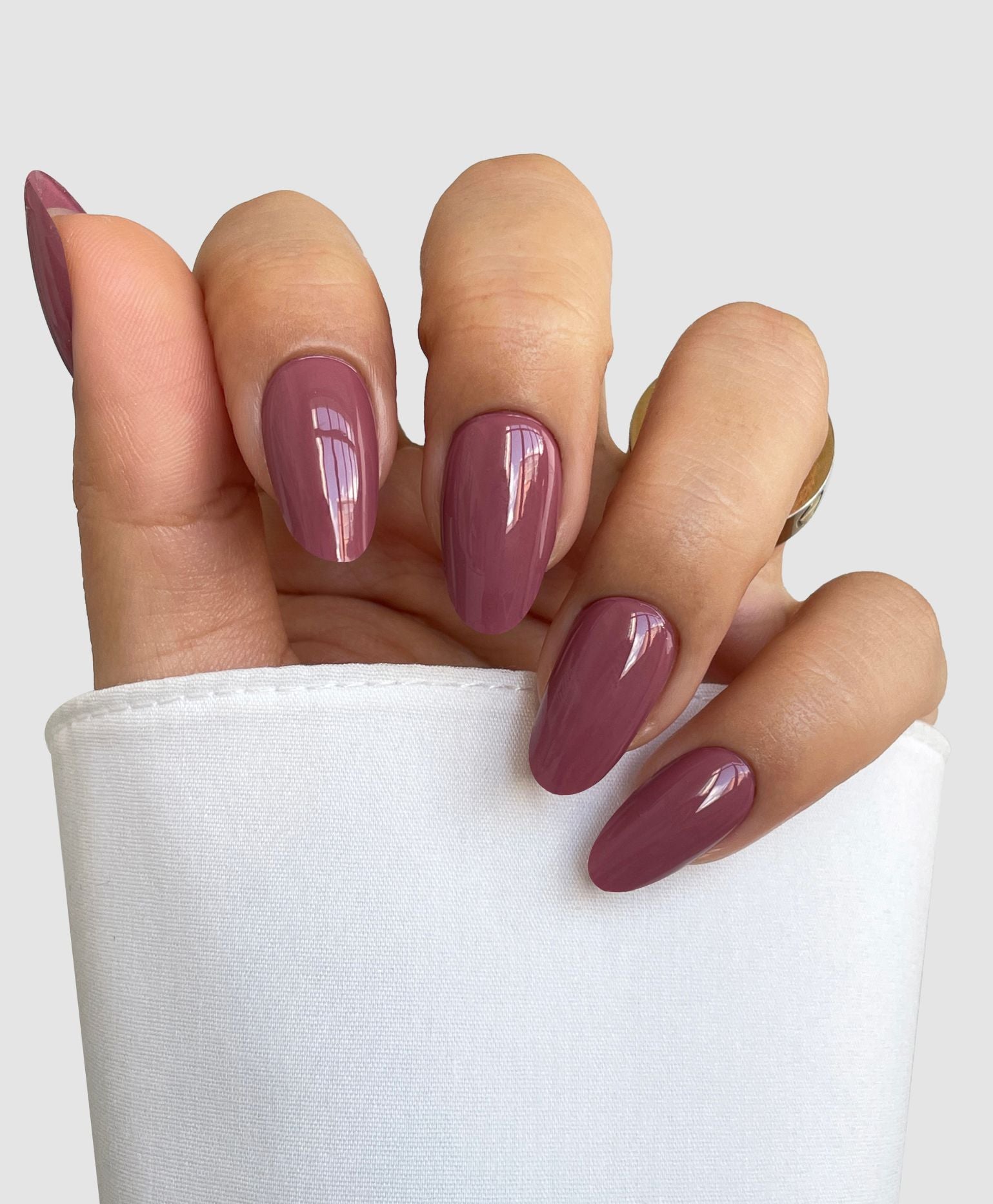 A hand with almond-shaped nails in Sassy Saints Deep Petal Gel Wrap, a glossy mauve shade, is partially covered by a white sleeve and set against a plain light gray background.