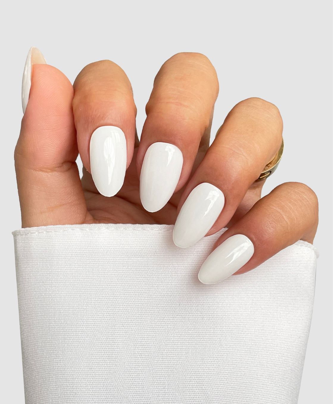 A hand with long, almond-shaped nails featuring Sassy Saints - Brings The Salon Home Coconut Milk Gel Wrap is shown against a light background, with a white sleeve and gold ring on the ring finger.