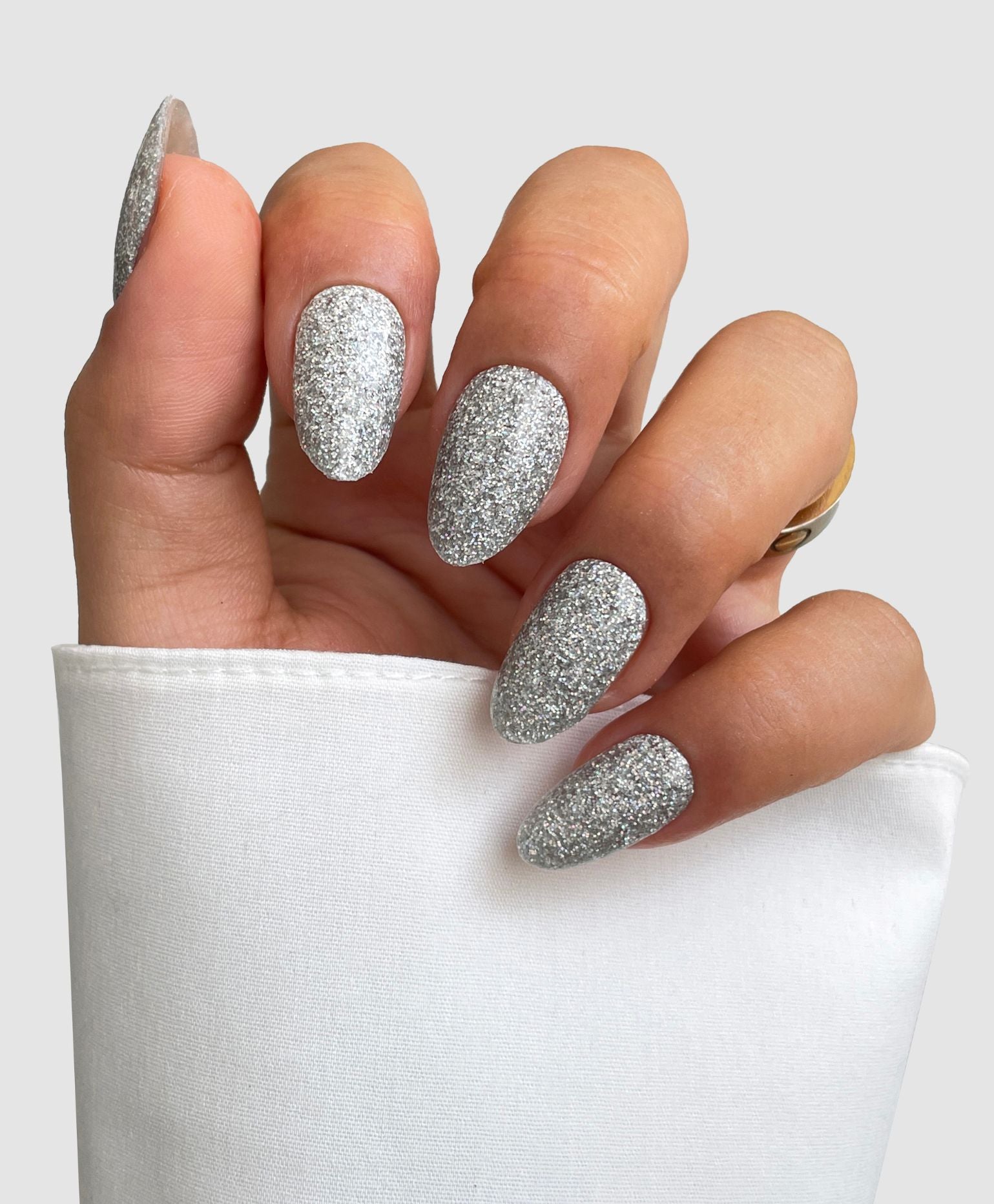 A hand with almond-shaped nails painted in Sassy Saints’ Liquid Platinum Gel Wrap gleams against a white fabric background, bringing the salon look home.