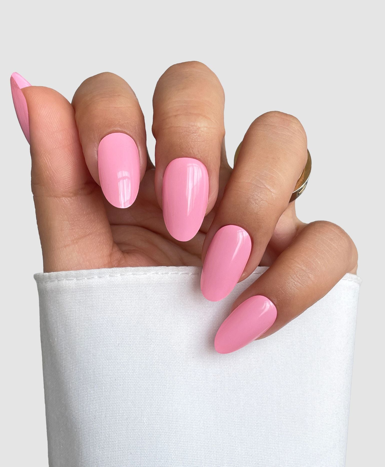 A hand with long, almond-shaped nails featuring Sassy Saints' Sugar Candy Gel Wrap, a glossy light pink, peeks from a white sleeve against a light gray background.