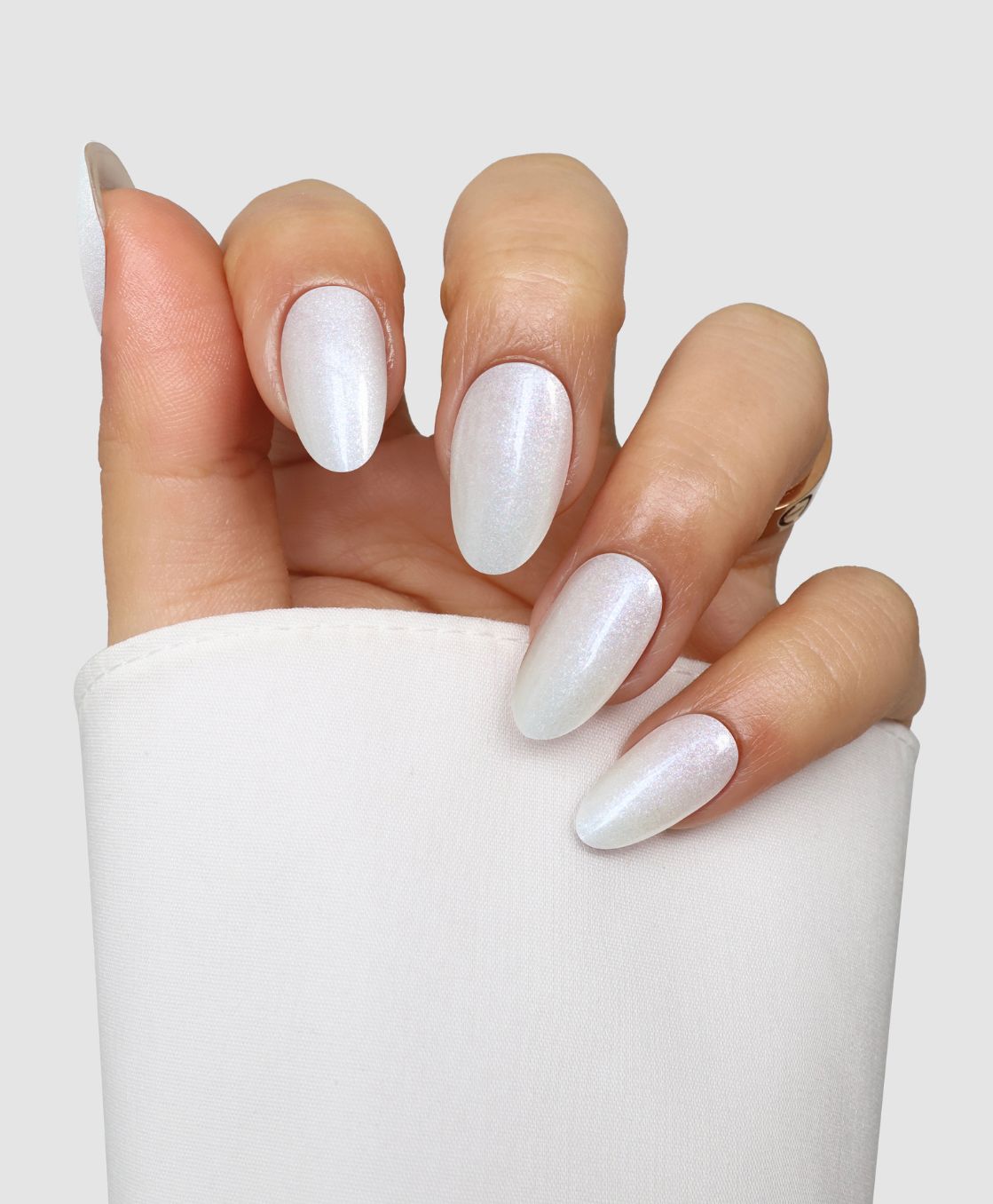 A hand with almond-shaped nails coated in Sassy Saints' Icy Veil Gel Wrap, shimmering white, peeks from a white sleeve against a light backdrop.