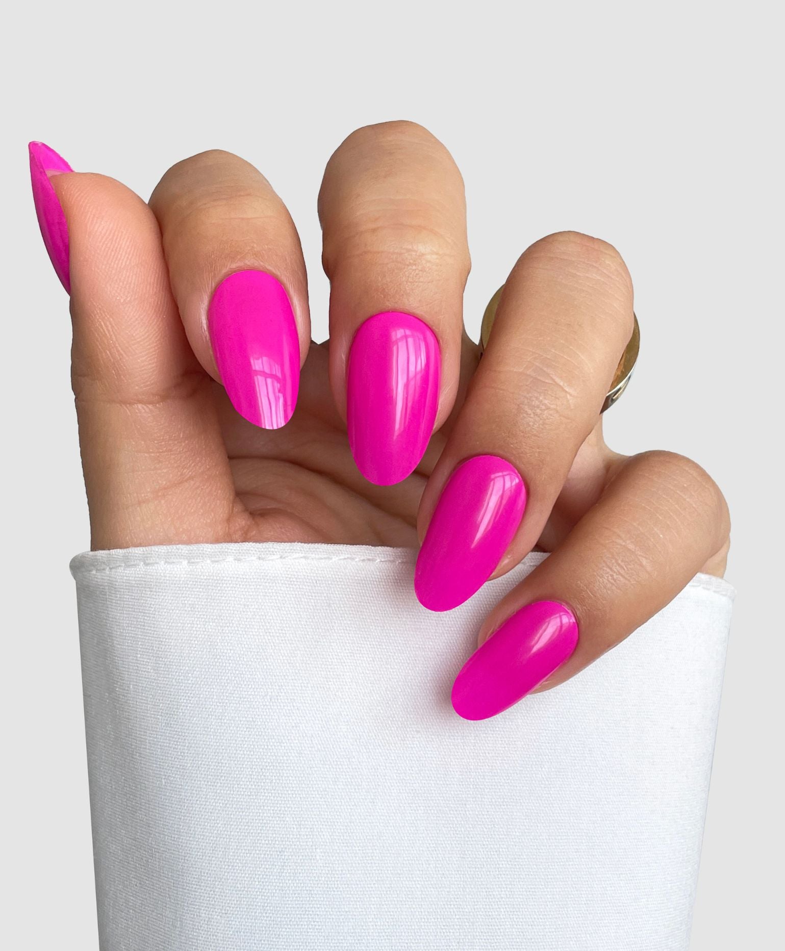 A hand with almond-shaped nails coated in Sassy Saints - Brings The Salon Home’s Pink Hype Gel Wrap peeks from a white sleeve against a light gray background.