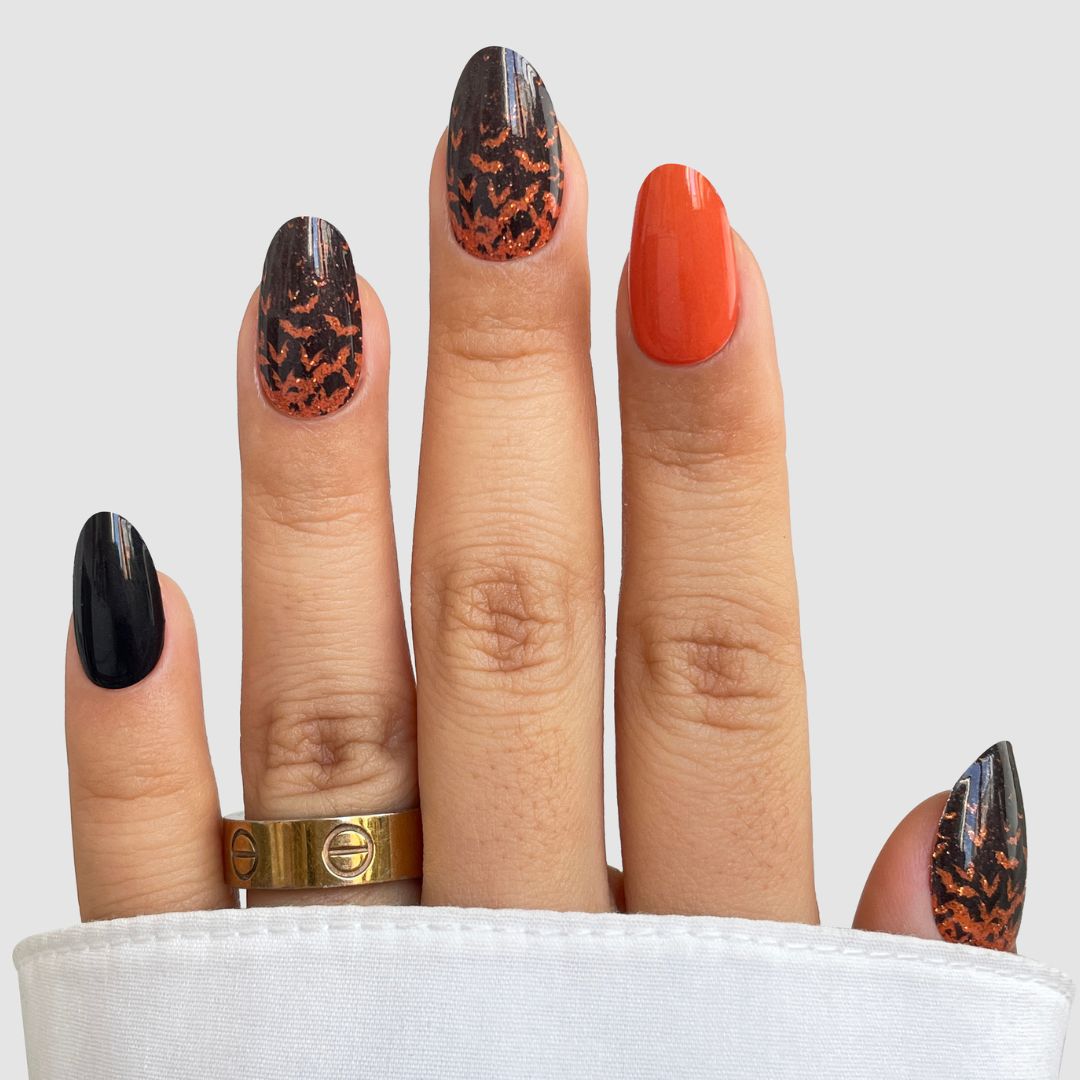 A hand displays Sassy Saints' Trick or Treat Gel Wraps: five nails with black, orange, and black-orange animal print designs. Two gold rings adorn the fingers, which are partially covered by a white sleeve.