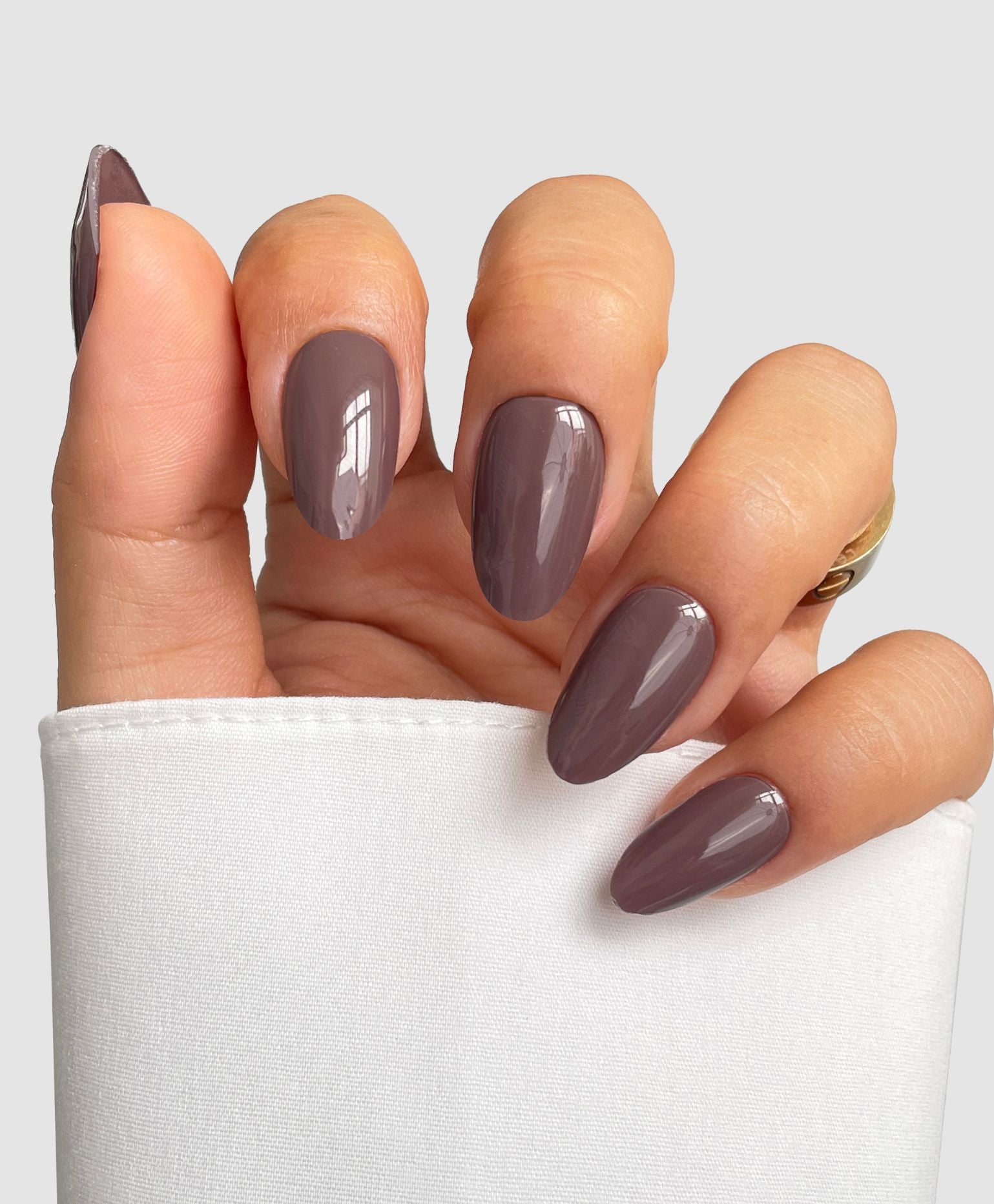 A hand with almond-shaped nails featuring Sassy Saints - Brings The Salon Home's Mocha Blend Gel Wrap, partially covered by a white sleeve, set against a light gray background.