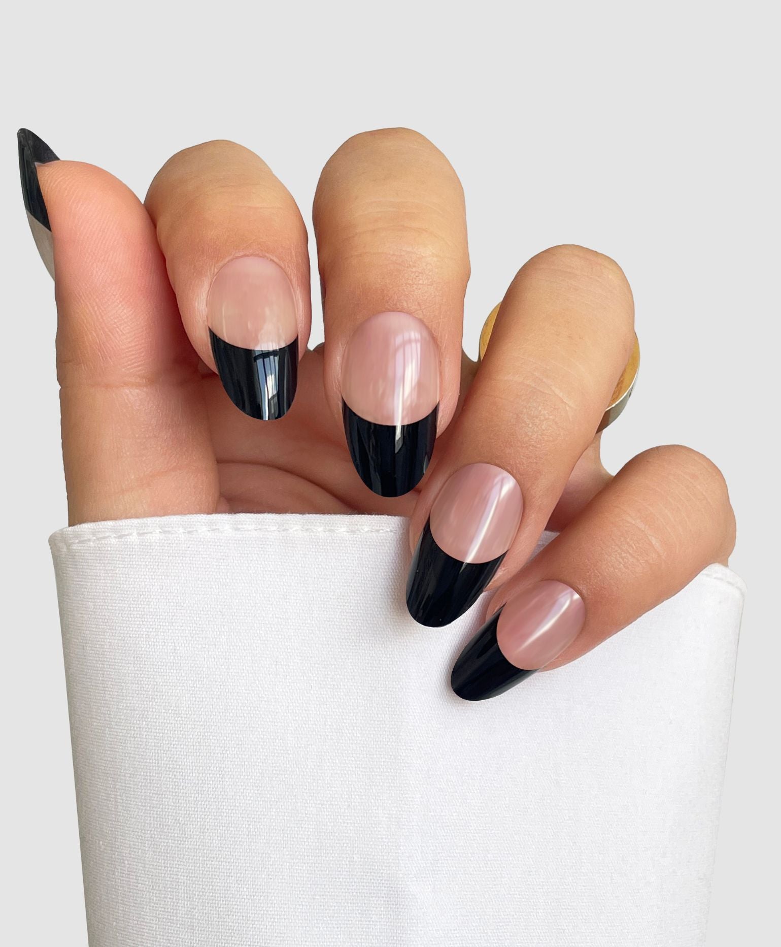 A hand with long, almond-shaped nails wears Sassy Saints' Midnight French Gel Wraps—featuring modern black tips and a natural pink base—resting against white fabric. Brings The Salon Home.