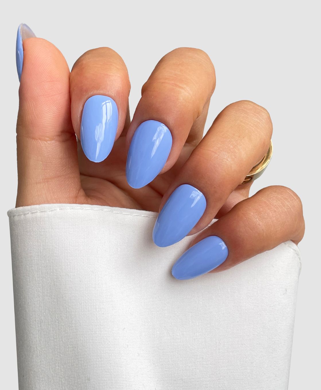 A hand with long, almond-shaped nails wears Sassy Saints' Iris Bleu Gel Wraps—a glossy lavender blue—partially wrapped in a white sleeve and adorned with a gold ring.