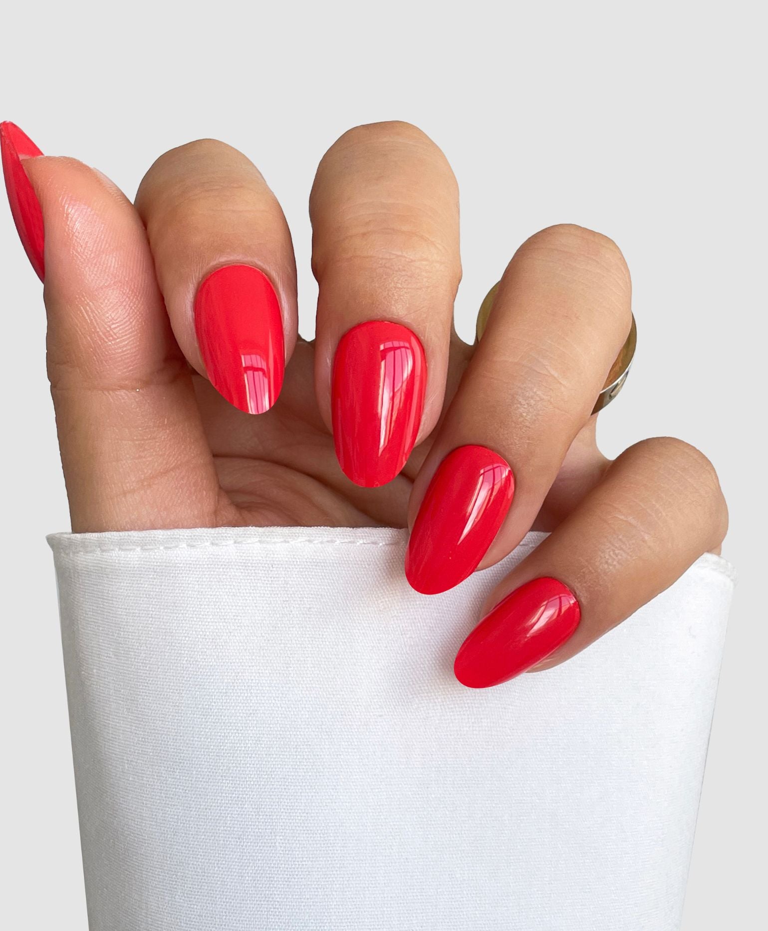 A hand with long, almond-shaped nails painted in Hotline Edit Gel Wrap by Sassy Saints – Brings The Salon Home, partially wrapped in white fabric against a light gray background.