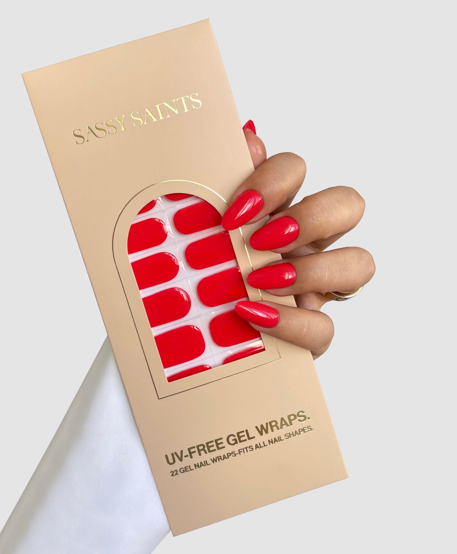 A hand with bright red nails holds a Sassy Saints - Brings The Salon Home Hotline Edit Gel Wrap package, displaying red gel nail wraps against a light gray background.