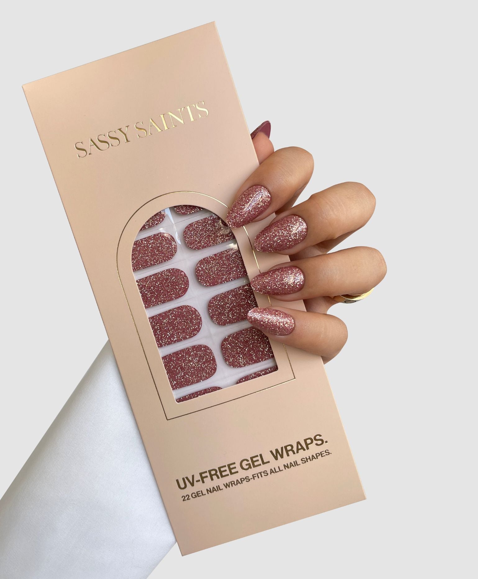 A hand with glittery pink Rose Spark Gel Wraps by Sassy Saints - Brings The Salon Home holds a box, revealing 22 sparkly gel wraps inside against a light background.