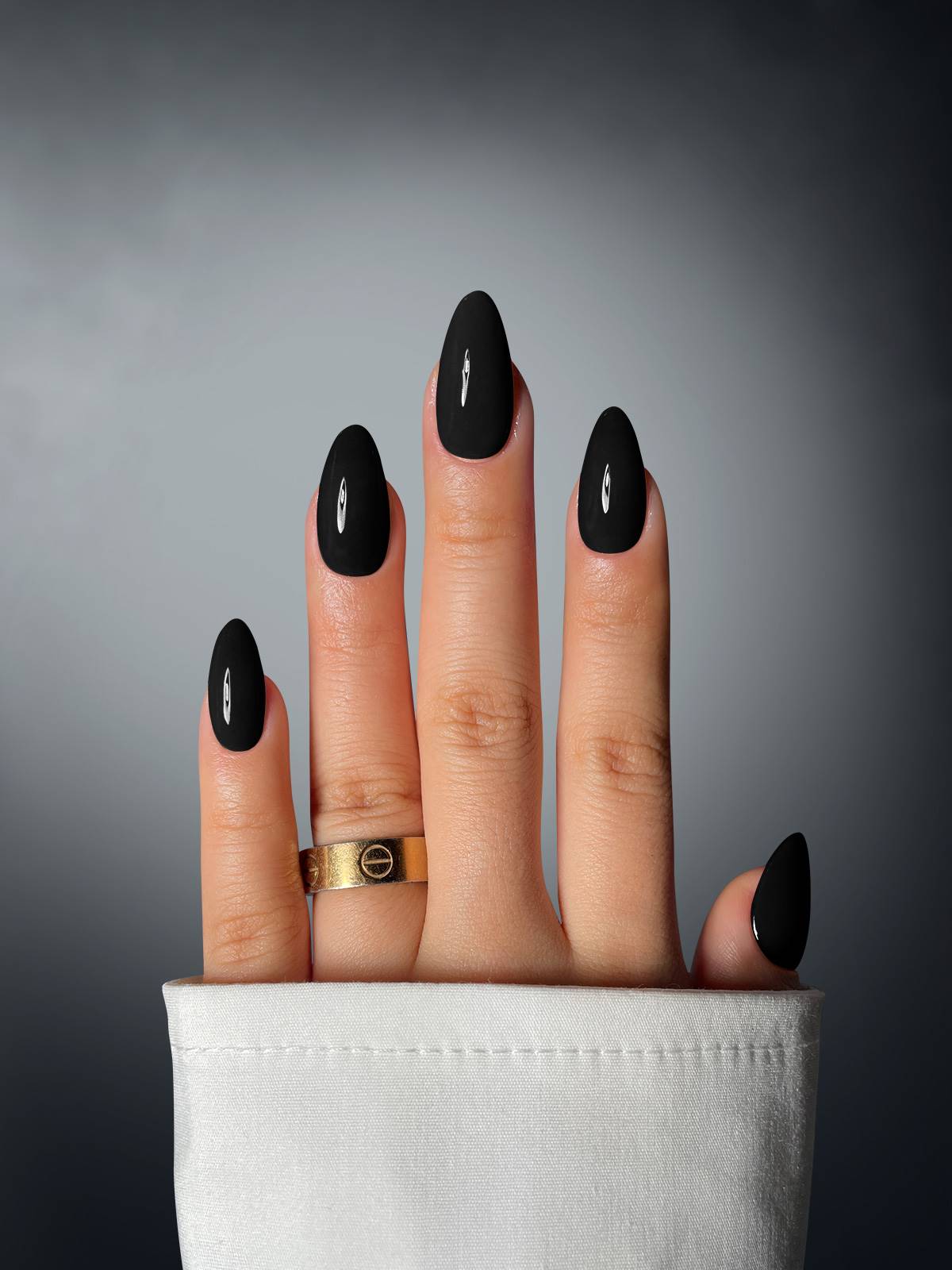 A hand with four fingers, each featuring Sassy Saints' Midnight Muse Dipping Powder in matte black with silver accents. A gold ring and a white sleeve complete the look against a gradient background.