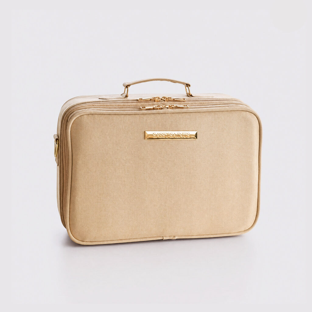A rectangular beige Beauty Bag by Sassy Saints - Brings The Salon Home, featuring a gold zipper, handle, and gold nameplate, serves as a stylish nail powder organizer or dip powder storage solution and is displayed on a plain white background.