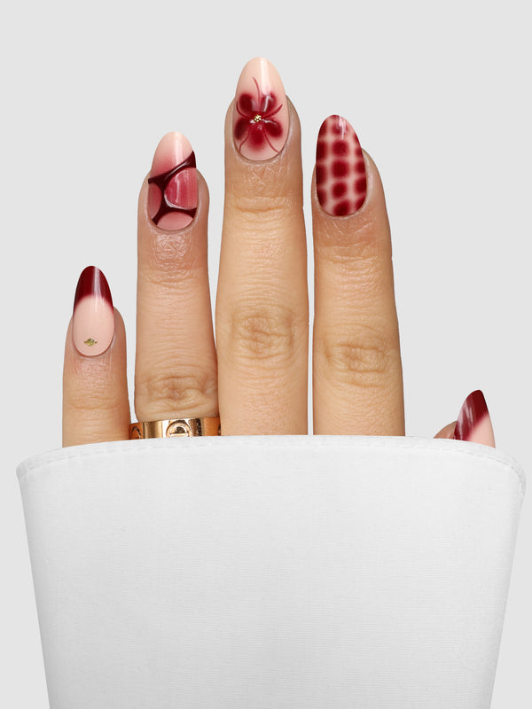 Burgundy Bloom (3D) Gel Wrap manicured fingernails featuring a mix of burgundy designs, including a flower, a geometric pattern, a French tip, and a checkered print.