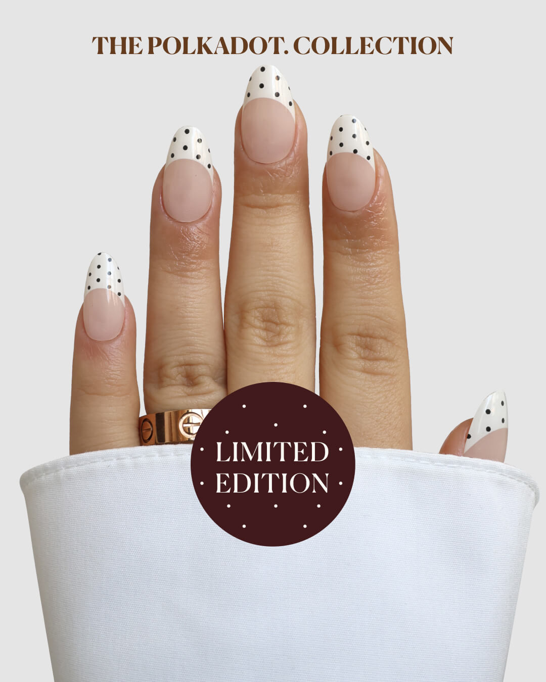A manicured hand shows Sassy Saints’ French with Benefits Gel Wrap: white tips with black polka dots, gold ring, white sleeve. Text on a brown circle reads THE POLKADOT. COLLECTION and LIMITED EDITION.