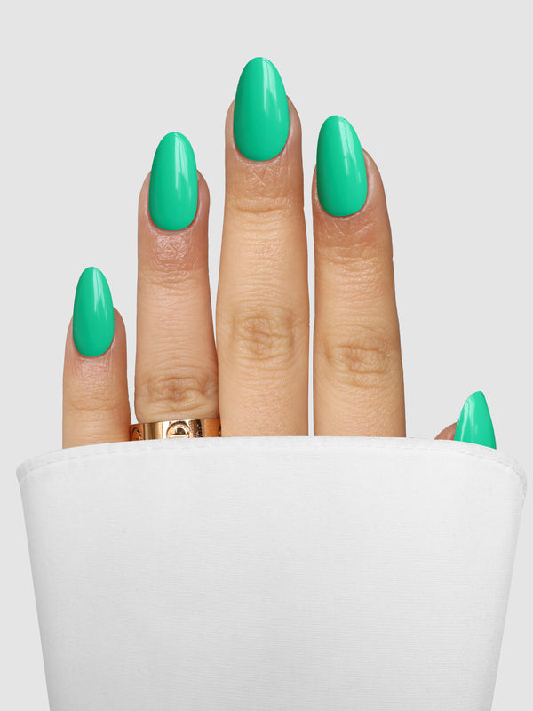 A hand with almond-shaped nails featuring Green Glow Gel Wrap in a vibrant green, wearing a gold band ring.