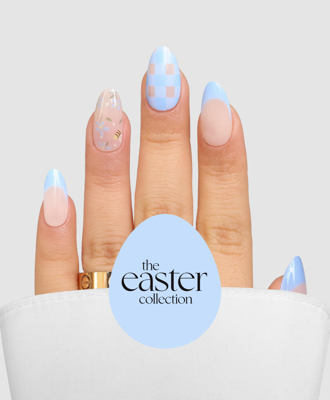 A hand displays the Sassy Saints - Brings The Salon Home Easter Picnic pastel nail art with blue and pink checkerboard, florals, and French tips, partly draped by a white cloth beside a blue egg labeled "the easter collection.