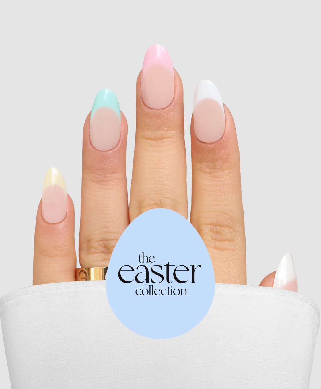 A hand with long, almond-shaped nails in Sassy Saints’ Pastel Parade—yellow, mint, pink, and white—emerges from a white cloth. A blue egg shape with “the easter collection” is overlaid at the bottom center.
