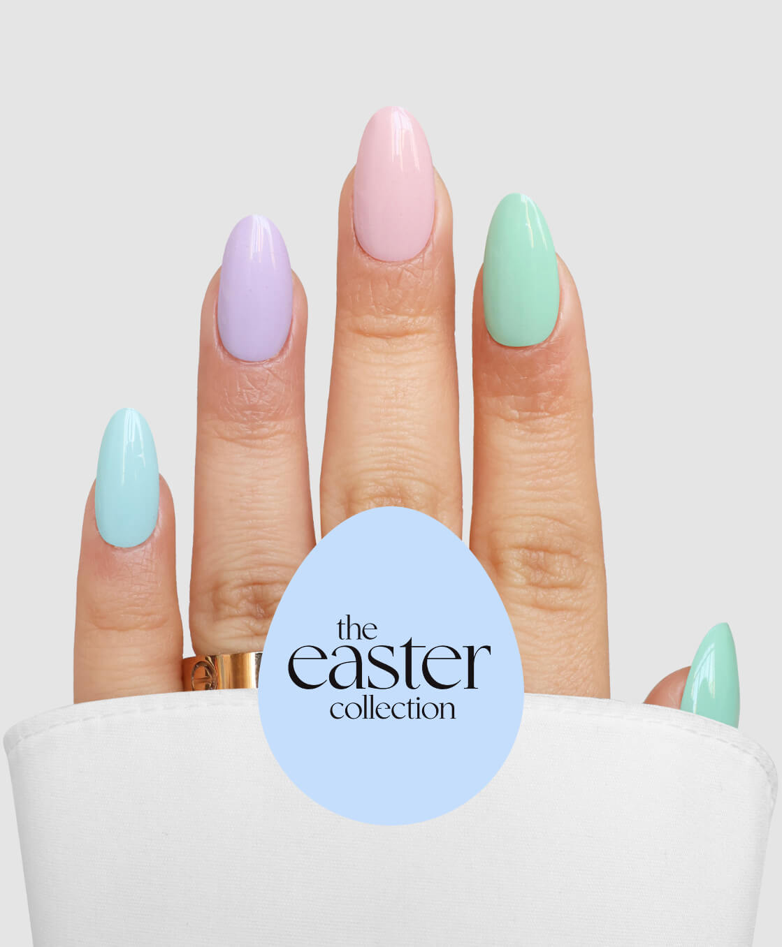 A hand with long, oval nails painted in pastel blue, purple, pink, green, and mint from the Hop Into Spring collection by Sassy Saints - Brings The Salon Home. Text on a blue egg reads "the easter collection." A white cloth partly covers the hand.