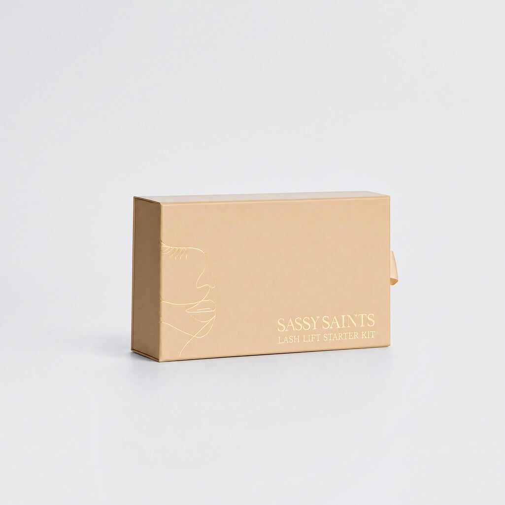 A light brown rectangular box labeled Lash Lift Mini Kit by Sassy Saints – Brings The Salon Home, featuring a simple line drawing of a face, promises beautifully lifted lashes and a long-lasting salon curl, displayed against a plain white background.