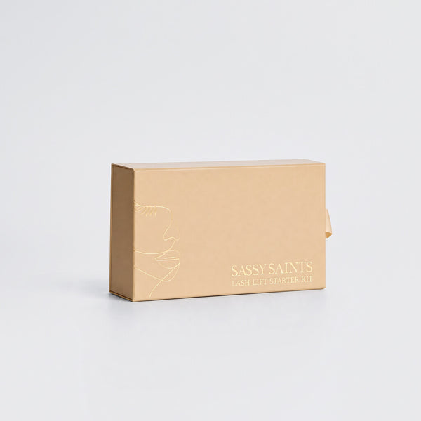 A light brown rectangular box labeled Lash Lift Mini Kit by Sassy Saints – Brings The Salon Home, featuring a simple line drawing of a face, promises beautifully lifted lashes and a long-lasting salon curl, displayed against a plain white background.