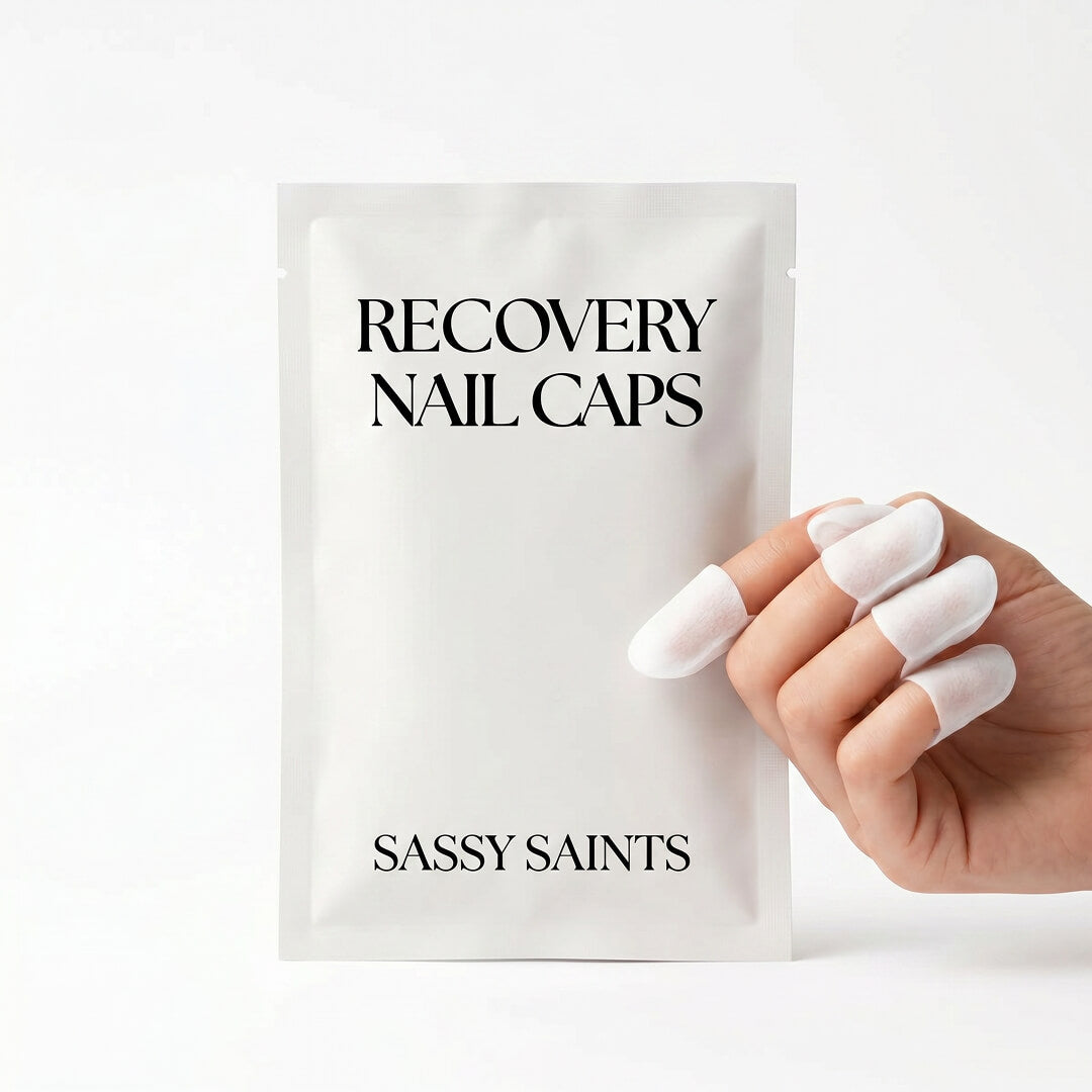 A hand wearing the white Nail Caps from Sassy Saints - Brings The Salon Home holds a packet labeled "RECOVERY NAIL CAPS" against a plain white background.