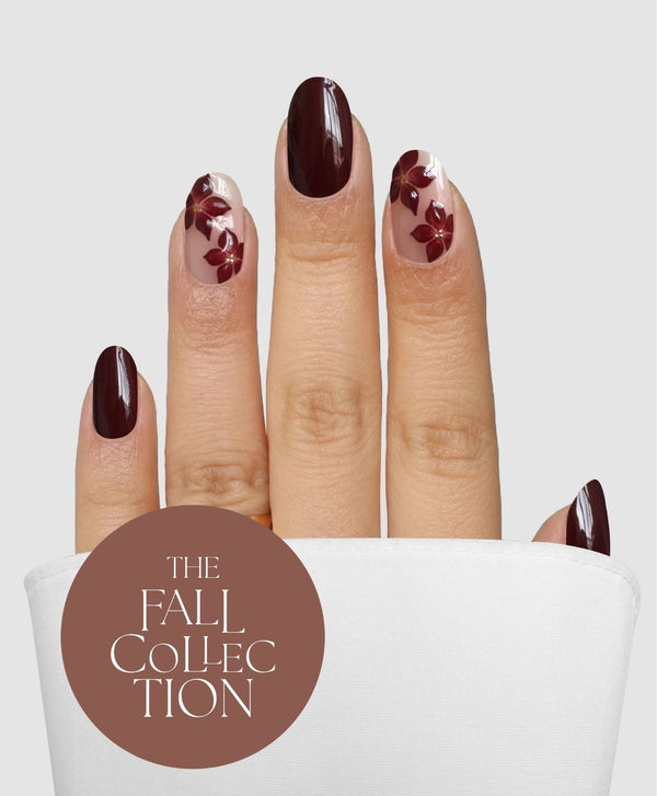 A hand with Sassy Saints - Brings The Salon Home Cabernet Corsage Gel Wraps—dark maroon nails adorned with floral designs on clear backgrounds—is partially draped in white fabric. The text “The Fall Collection” appears in a brown circle.