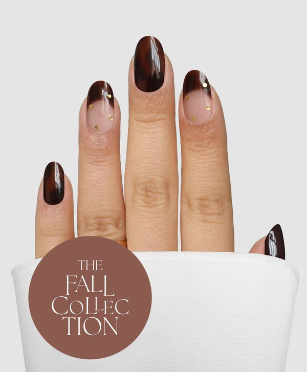 A hand with almond-shaped nails, styled in the Sassy Saints - Brings The Salon Home Tortoise Takeover Gel Wrap featuring a dark brown and nude ombre design with gold dot accents, is shown emerging from a white pocket. A brown circle at the bottom left reads, The Fall Collection.