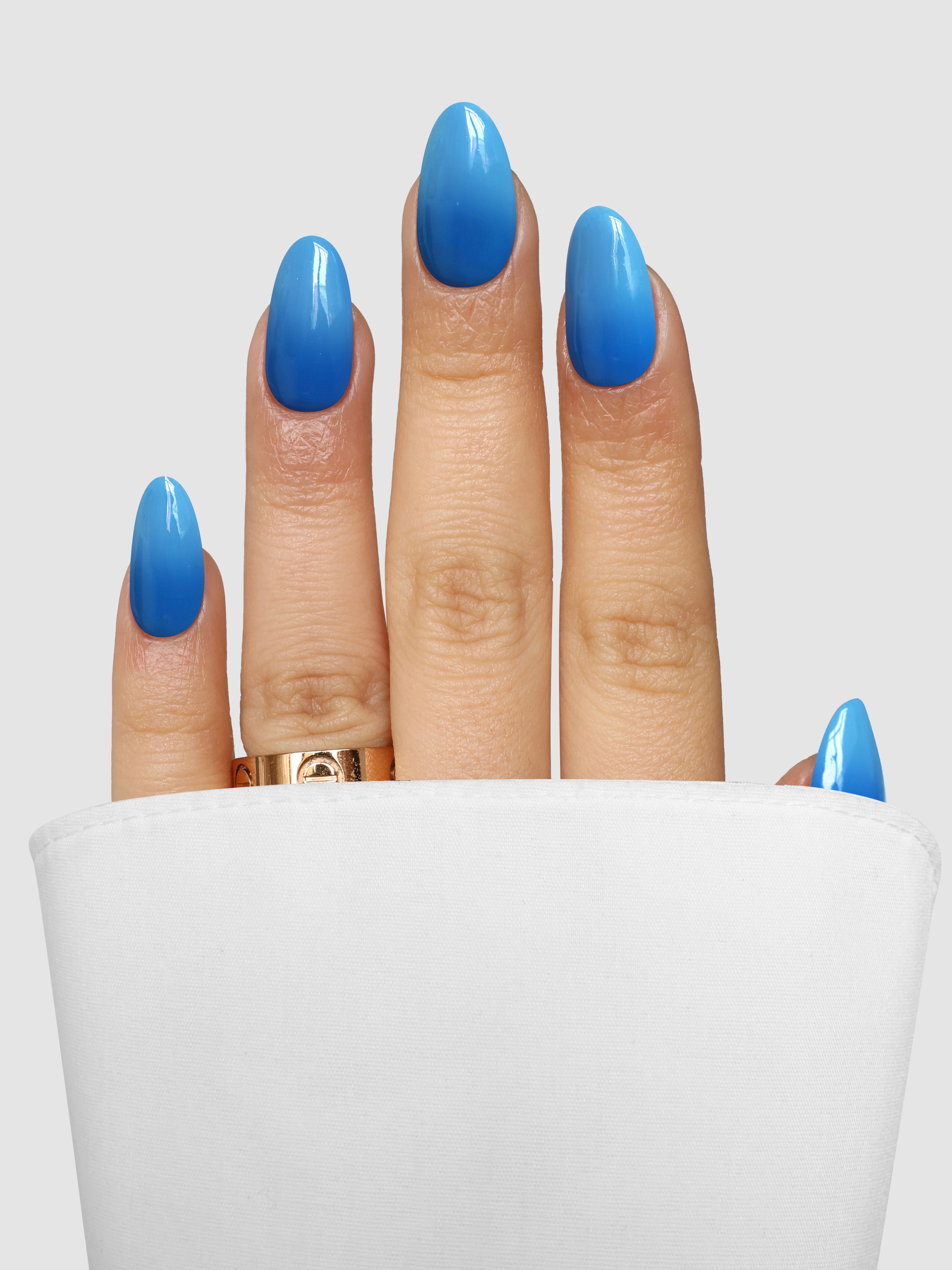 A hand with long, oval nails painted in Sassy Saints Navy Nimbus Dipping Powder peeks from a white sleeve. A gold ring adorns the middle finger, set against a light gray background.