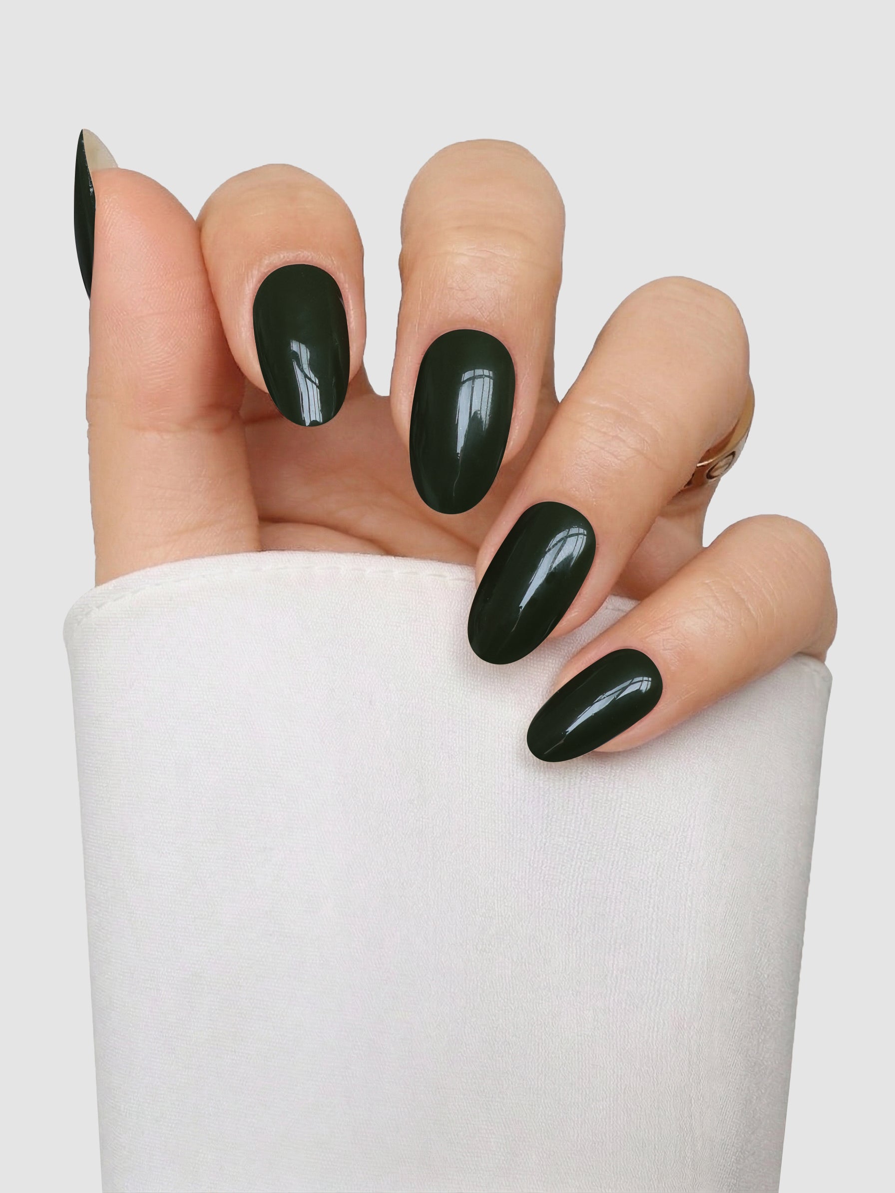 A hand featuring almond-shaped nails coated in Sassy Saints’ Olive Instinct Gel Wrap, glossy and dark green, is slightly curled against a white background. The person is dressed in a white long-sleeve garment.