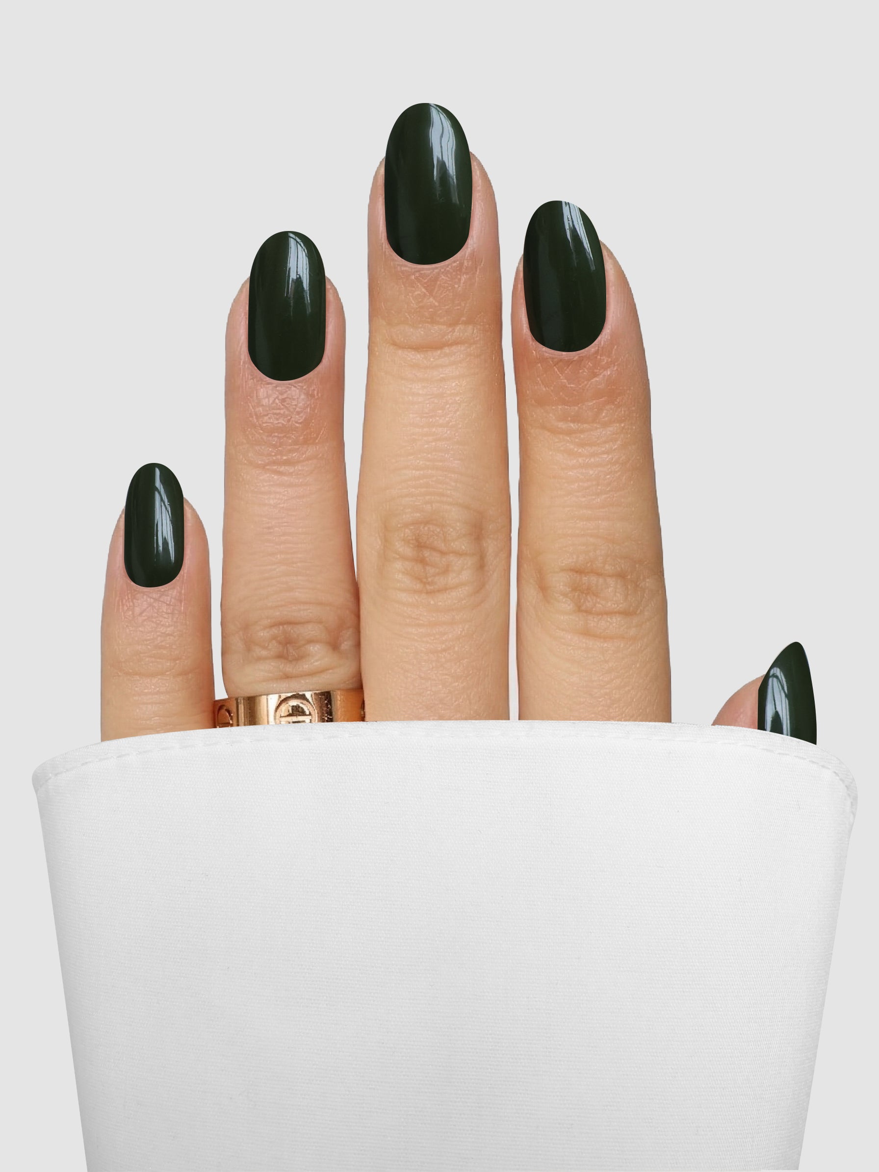 A hand with nails polished in Sassy Saints - Brings The Salon Home’s Olive Instinct Gel Wrap and adorned with a gold ring rests partially covered by white fabric against a light gray background.