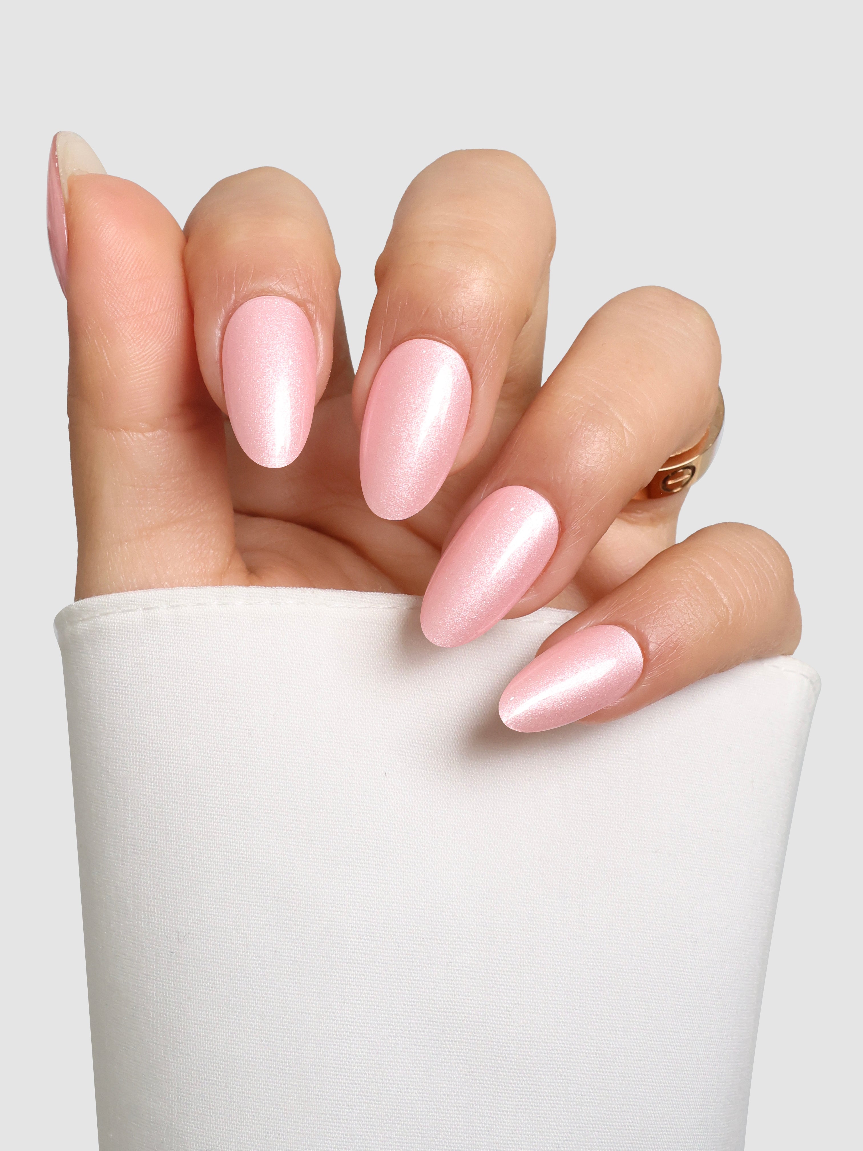 A hand with almond-shaped nails wears Sassy Saints Pop Crush Gel Wrap in glossy pastel pink, resting against a white fabric background.