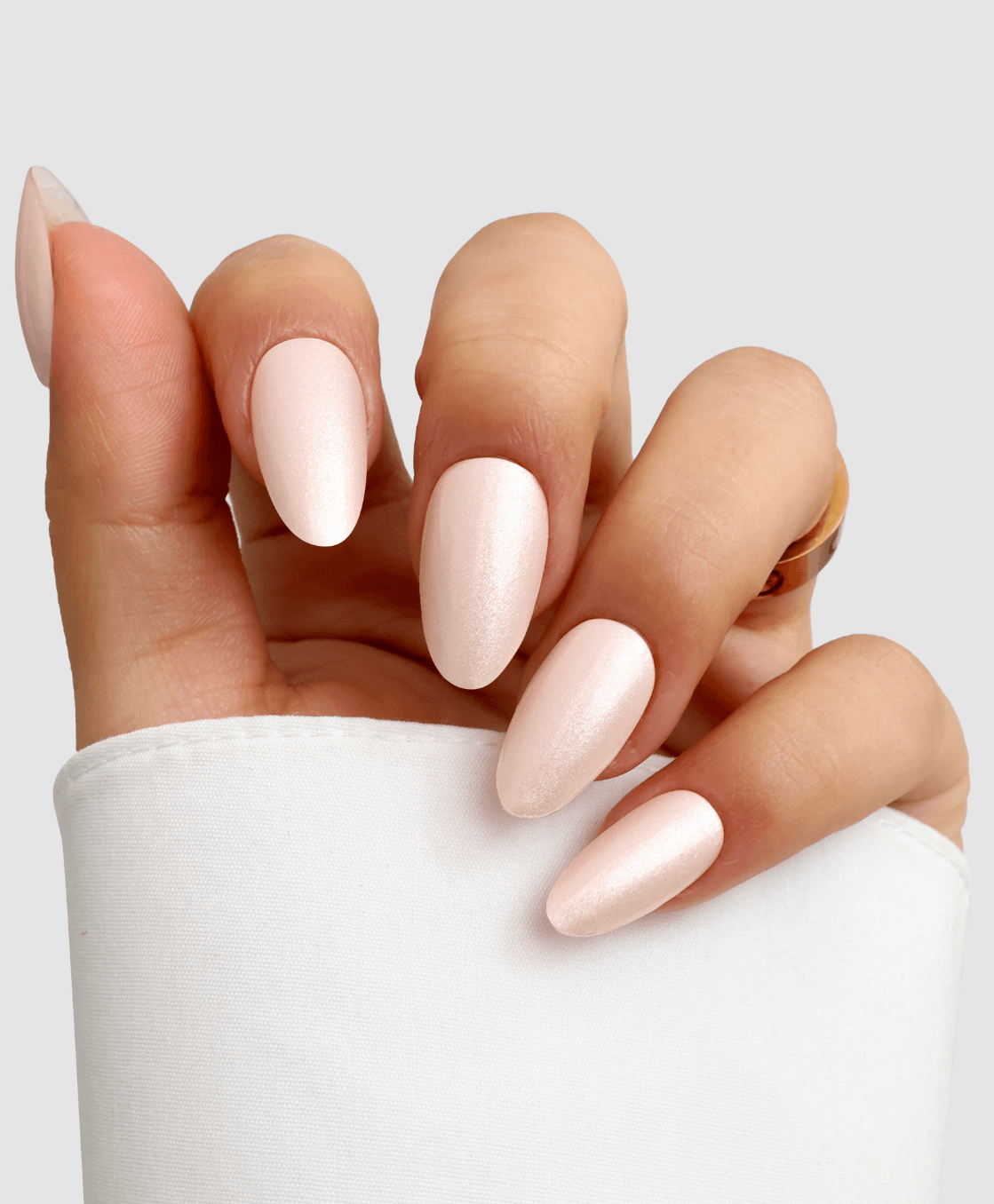 A hand with long, almond-shaped nails in shimmery pale pink Powder Puff Gel Wrap by Sassy Saints - Brings The Salon Home, partially covered by a white sleeve, against a light gray background.