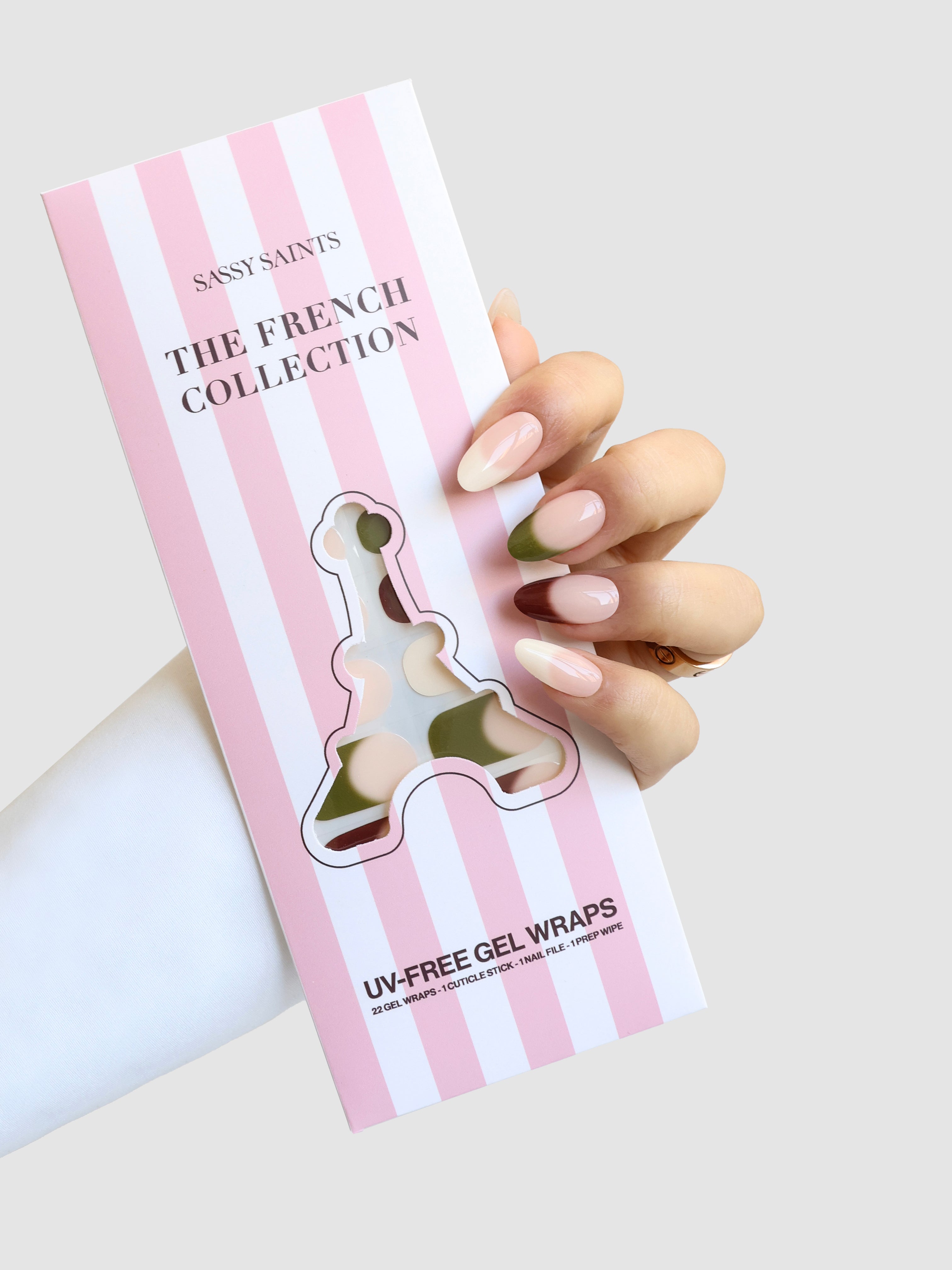 A hand with long, almond-shaped nude and pink French manicure nails holds a pink-and-white striped box labeled Sassy Saints - Brings The Salon Home Terre Chic Gel Wrap.