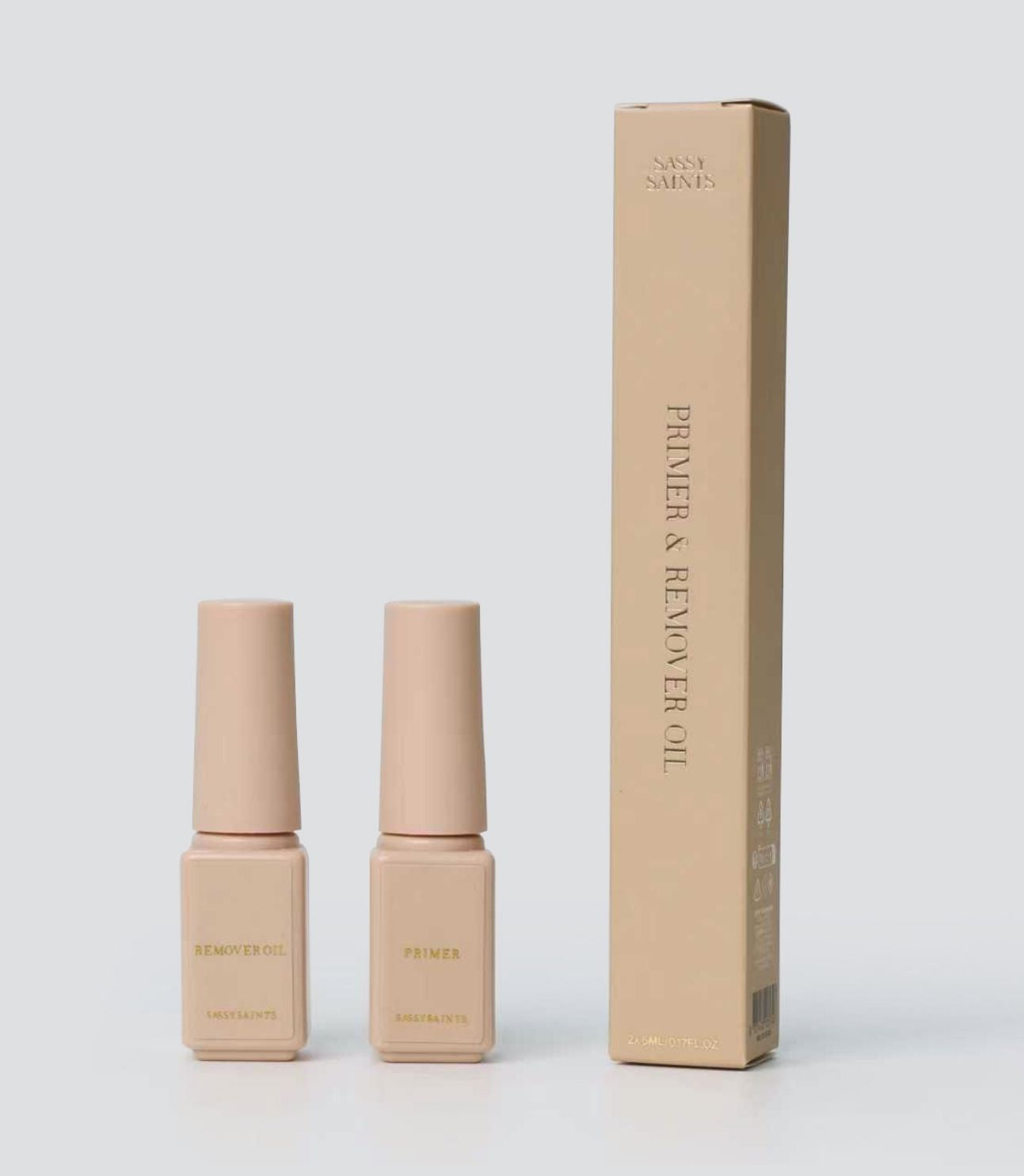 Two beige bottles labeled Primer and Remover Oil from the Sassy Saints - Brings The Salon Home Primer & Remover Oil Bundle stand next to a matching beige box, all set against a plain light gray background.