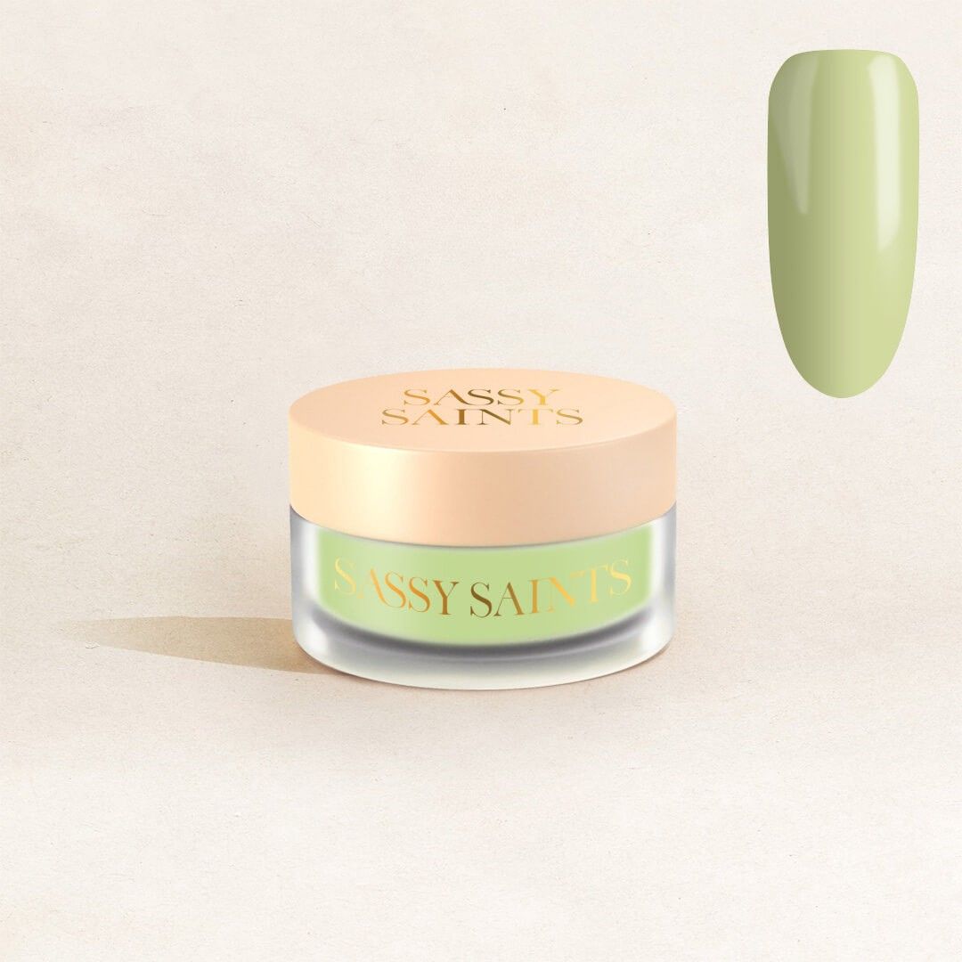 A small glass jar with a beige lid labeled "Sassy Saints - Brings The Salon Home" sits on a neutral background. In the upper right corner, a swatch of "Lush Lime Dipping Powder" nail color is displayed.