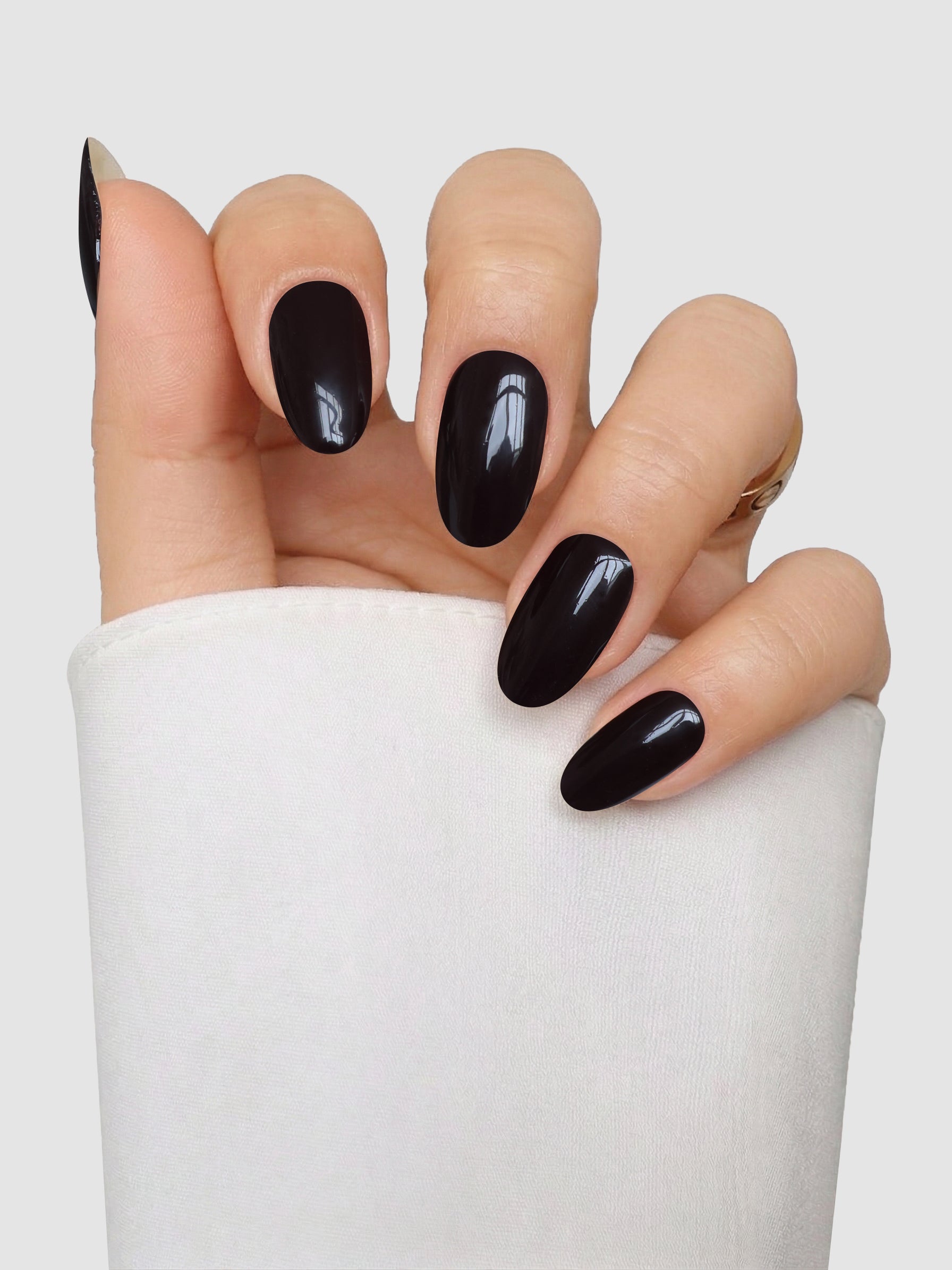 A hand with long, oval-shaped nails featuring the glossy black Velvet Vice Gel Wrap by Sassy Saints - Brings The Salon Home rests against a white sleeve, set against a light gray background.