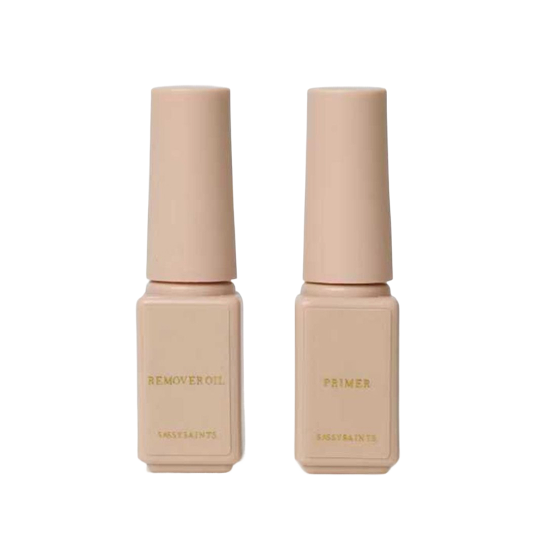 Two beige rectangular bottles labeled “REMOVER OIL” and “PRIMER” in gold, from Sassy Saints’ Primer & Remover Oil Bundle (FREE), shown against a plain white background.